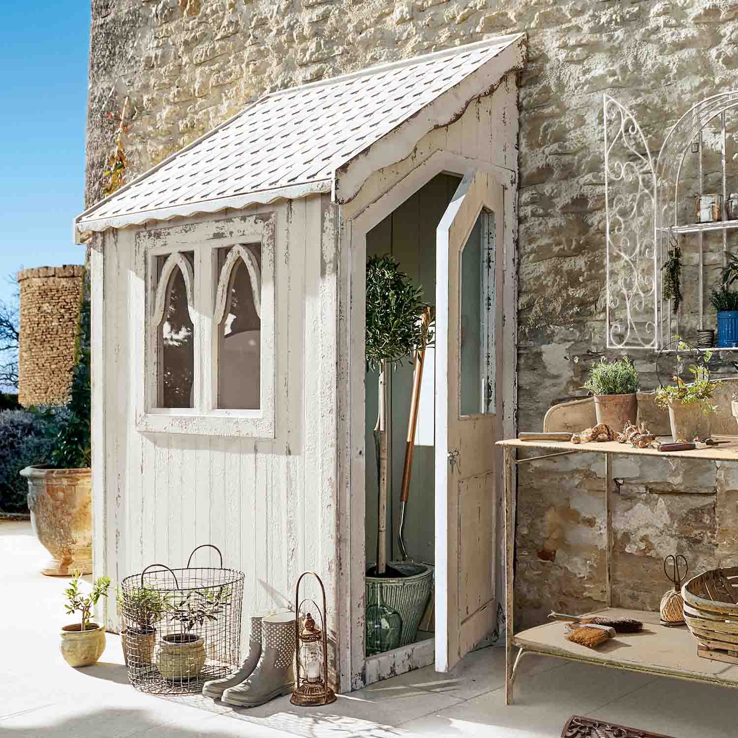Witte houten tuinhuisje met ramen en open deur, tuinaccessoires en gereedschap