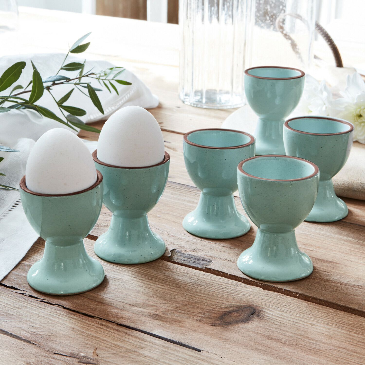 Set van zes lichtblauwe keramische eierdopjes met bruine rand op rustieke houten tafel