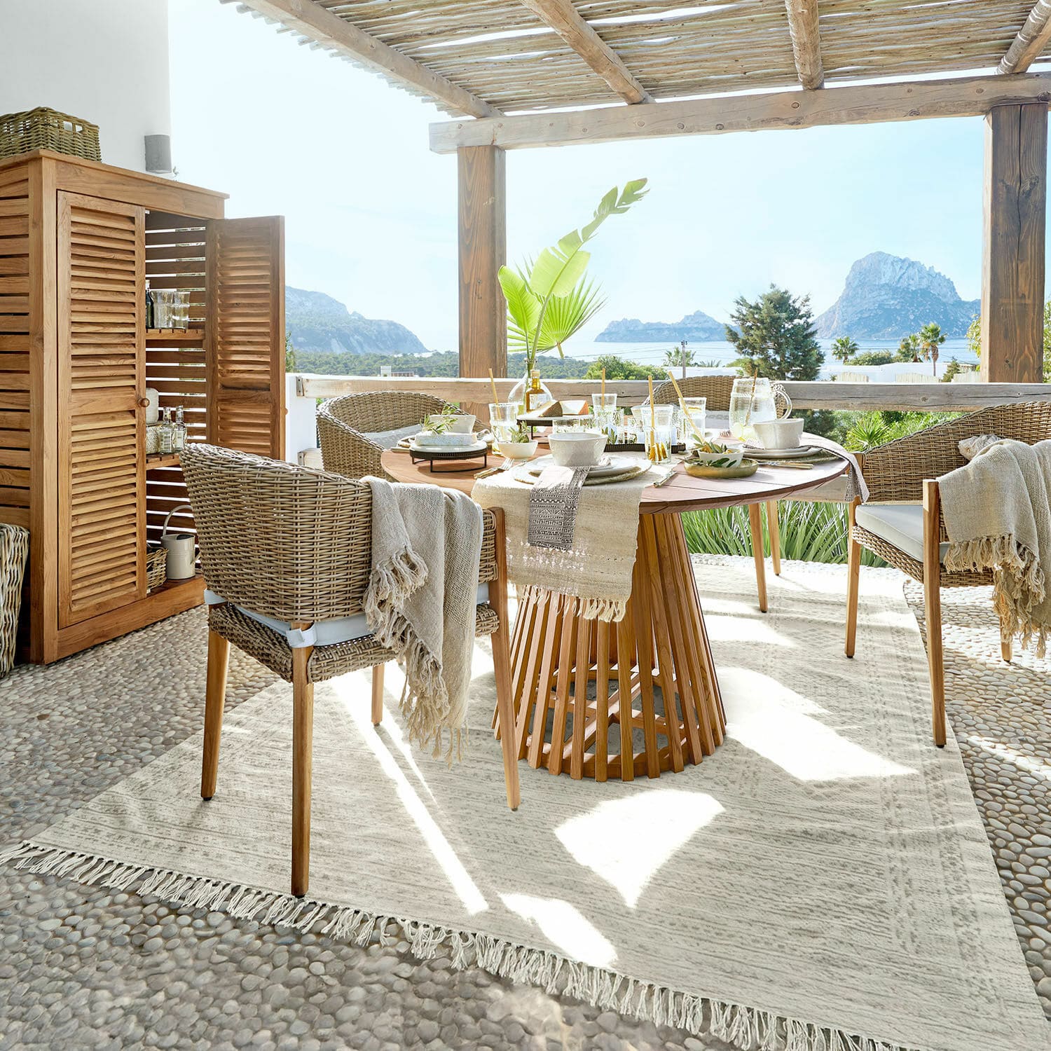 Vloerkleed voor buiten Savagnac Eethoek op terras met houten tafel en beige rotan stoelen, uitzicht op zee en natuurlijke inrichting