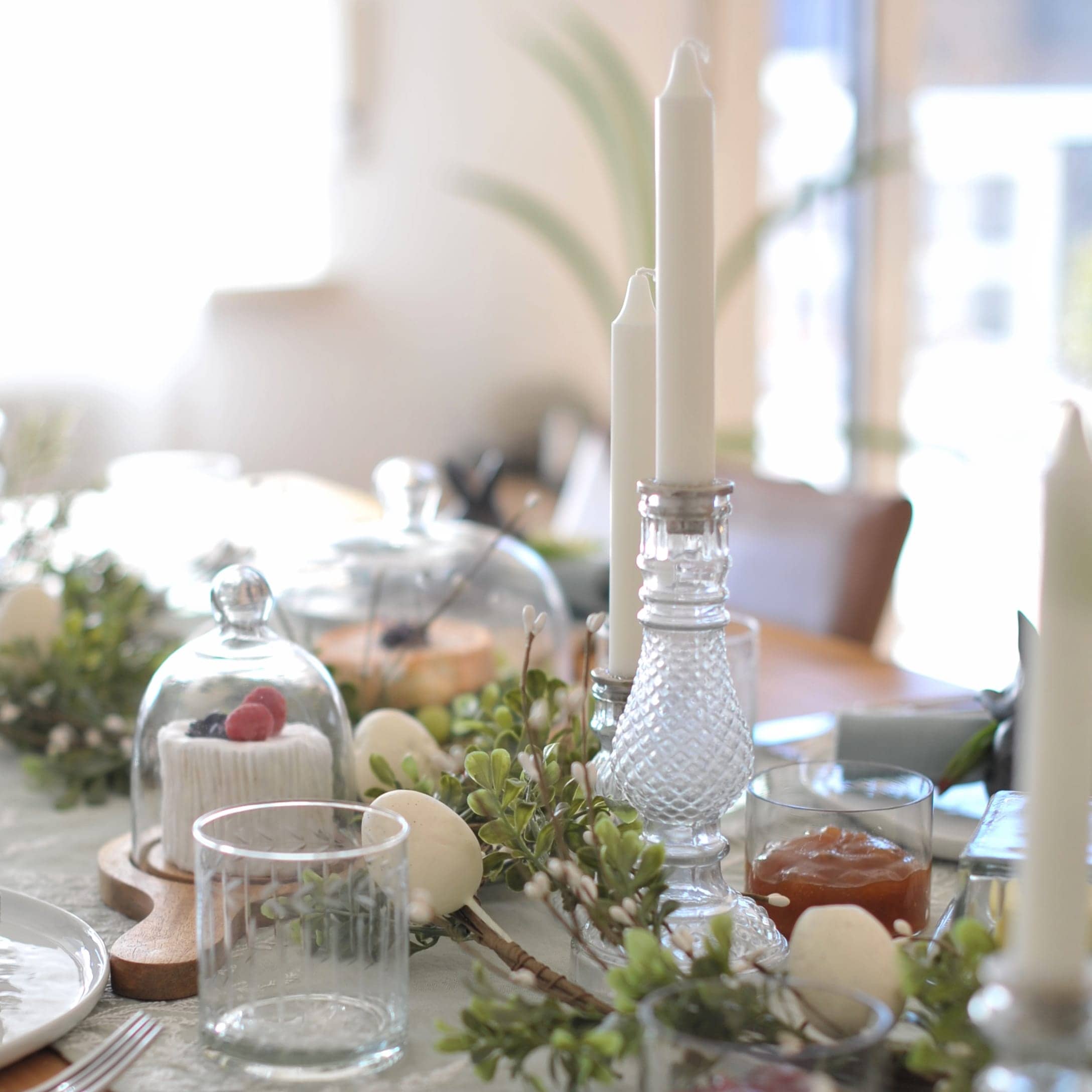 Feestelijk gedekte tafel met witte kaarsen in glazen kandelaars en groene takken als decoratie