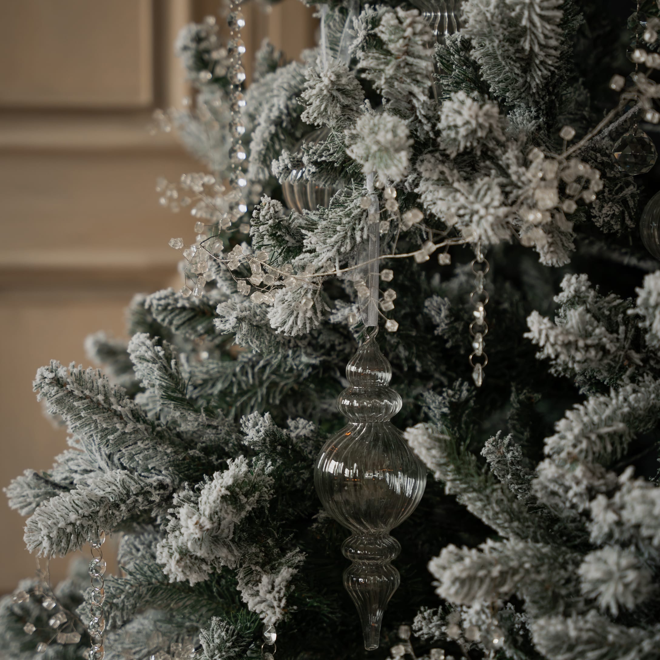 Close-up van groene, besneeuwde kunstkerstboom met transparante glazen kerstversiering