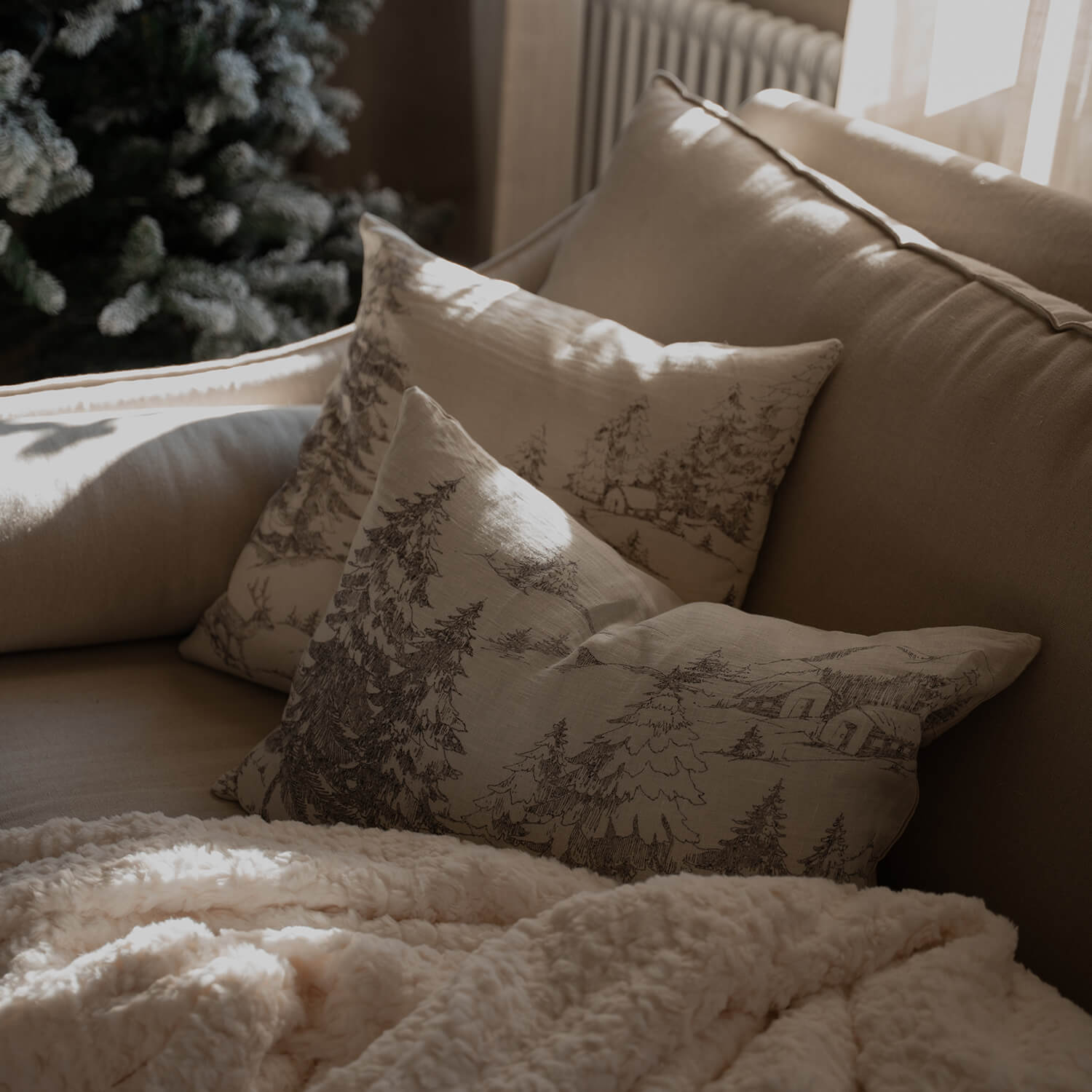 Beige bank met decoratieve kussens met bosmotief en zachte crèmekleurige deken in woonkamer