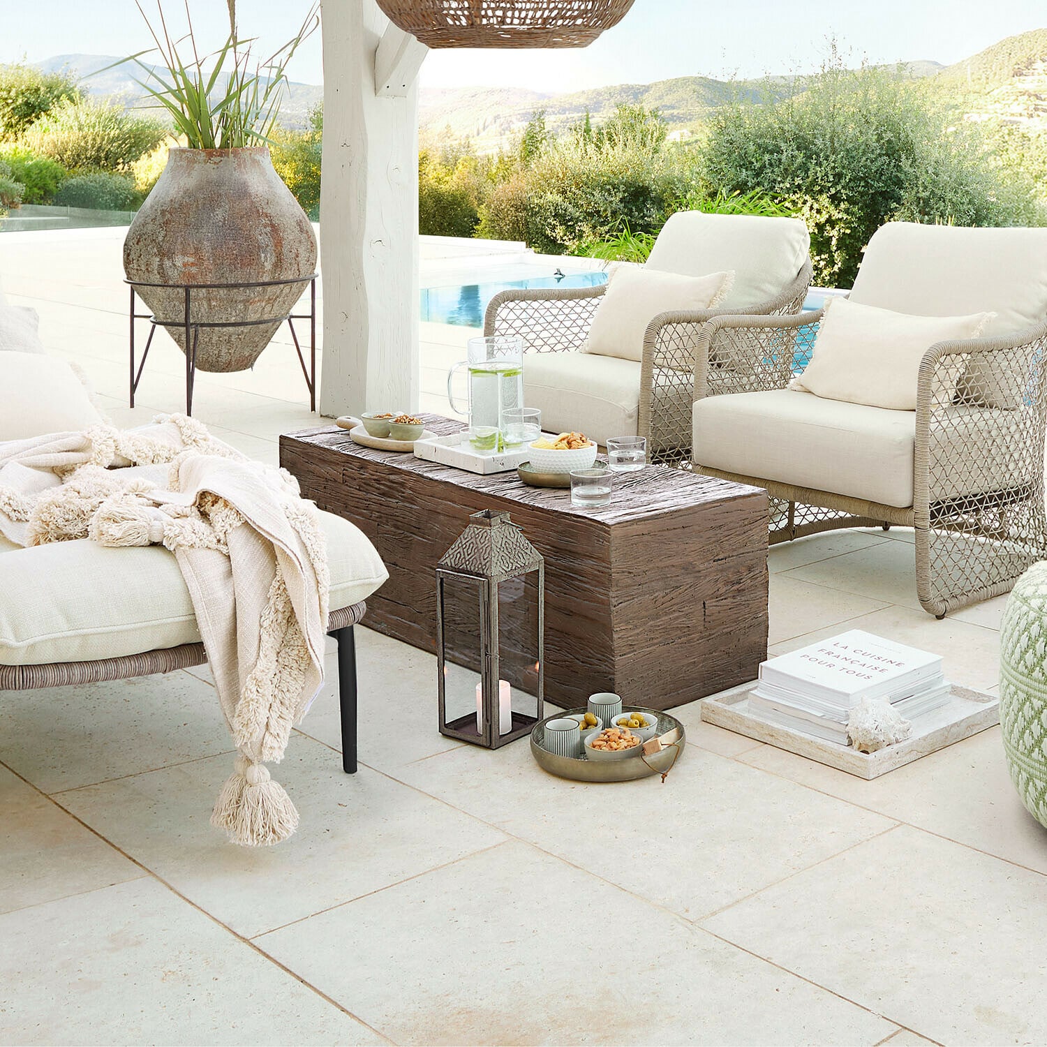 Gezellige tuinmeubels met beige kussens en houten tafel op terras met uitzicht op zwembad en natuur