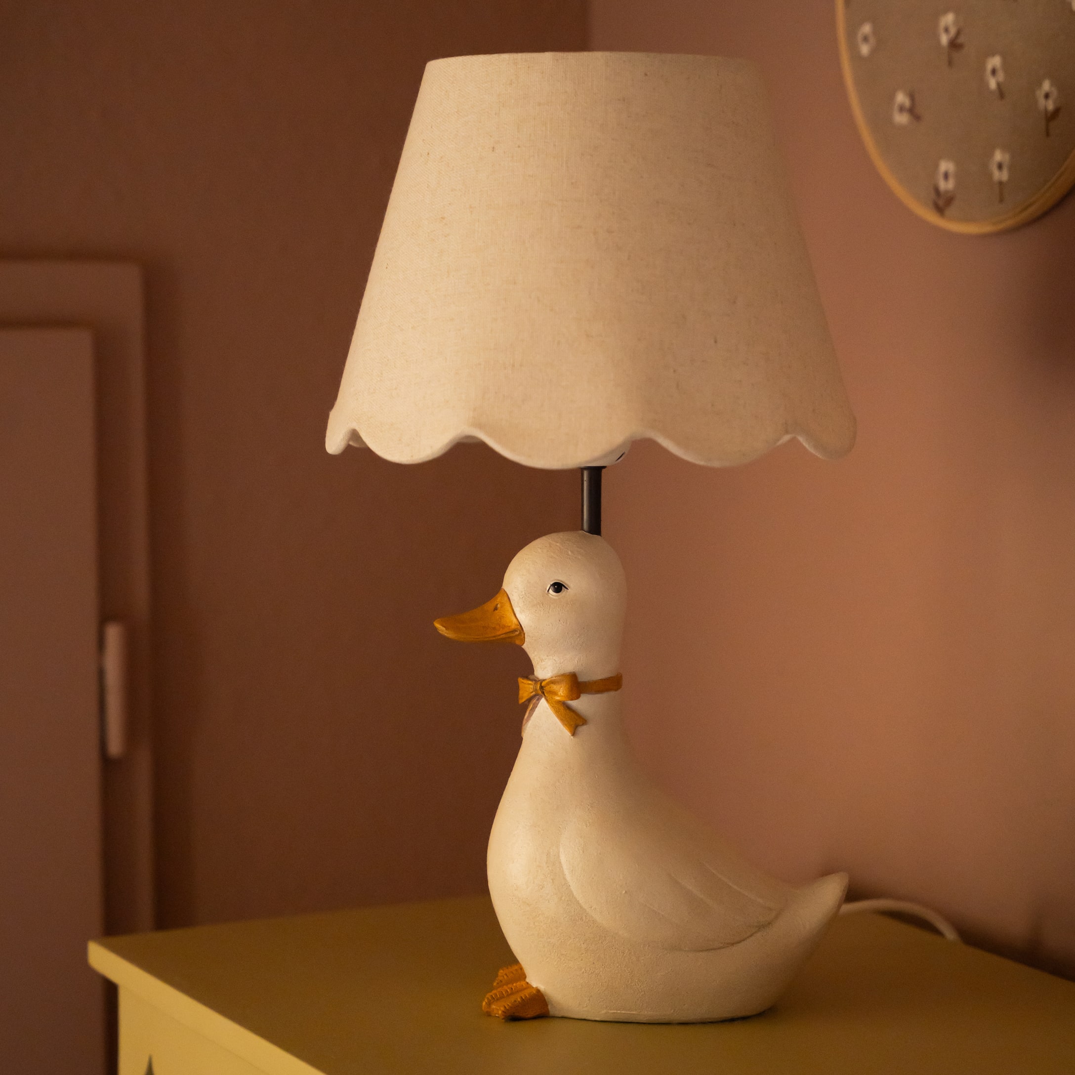 Tafellamp in de vorm van een witte eend met een beige lampenkap en een oranje decoratieve strik