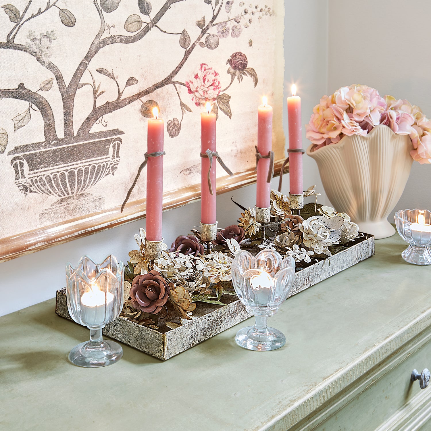 Decoratieve kandelaar met metalen bloemen en roze kaarsen op groene kast met vaas
