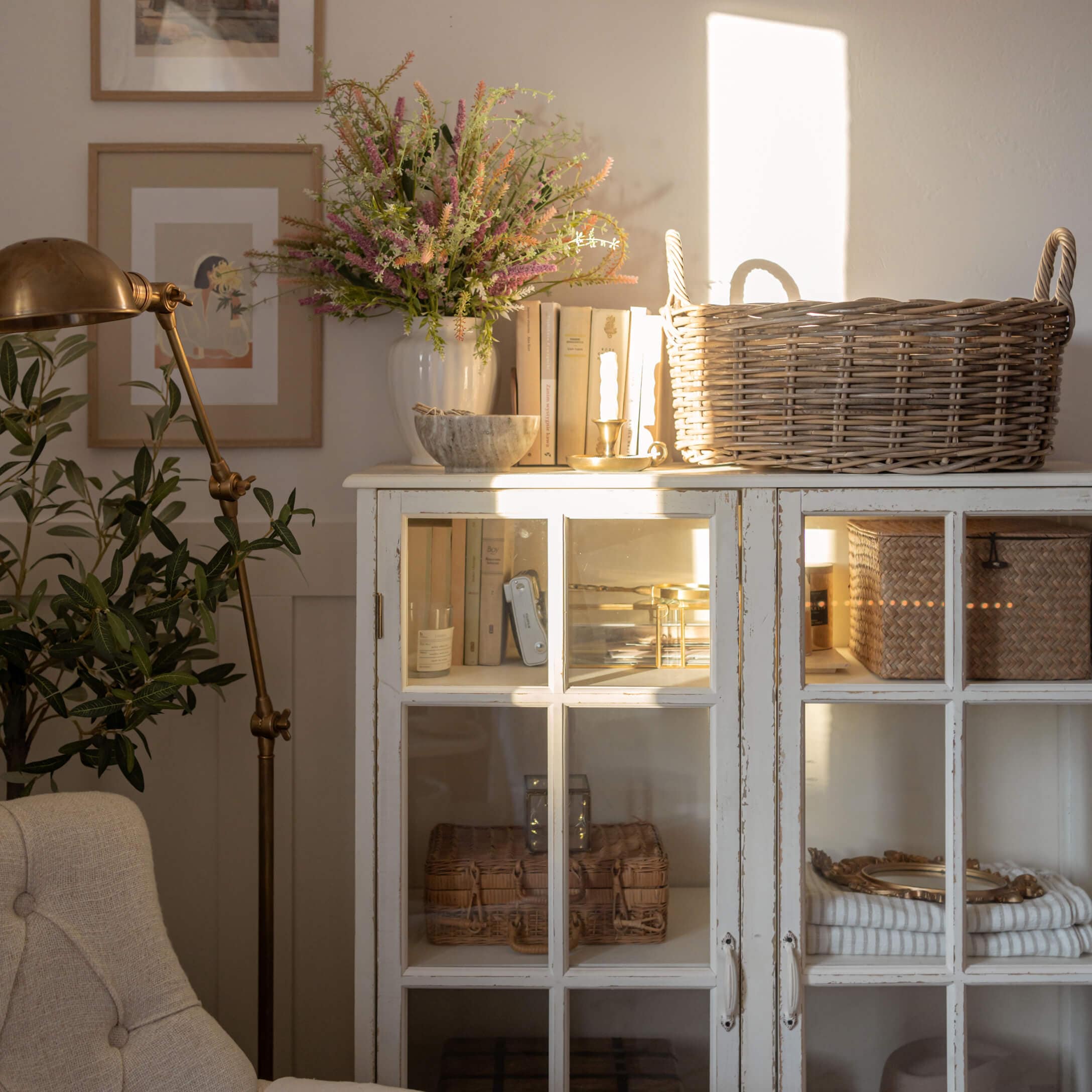 Witte houten kast met glazen deuren, rieten mand en decoratie in lichte woonkamer