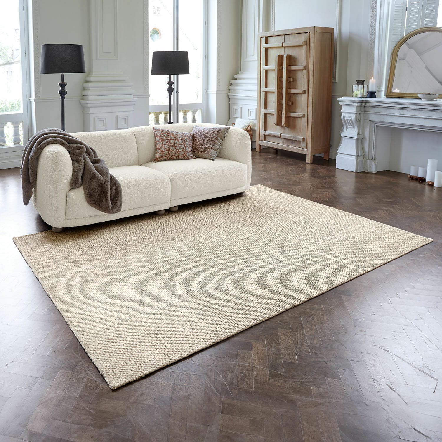 Vloerkleed Coleman Beige vloerkleed van natuurlijke vezels in moderne woonkamer met crèmekleurige bank en donkere houten vloer
