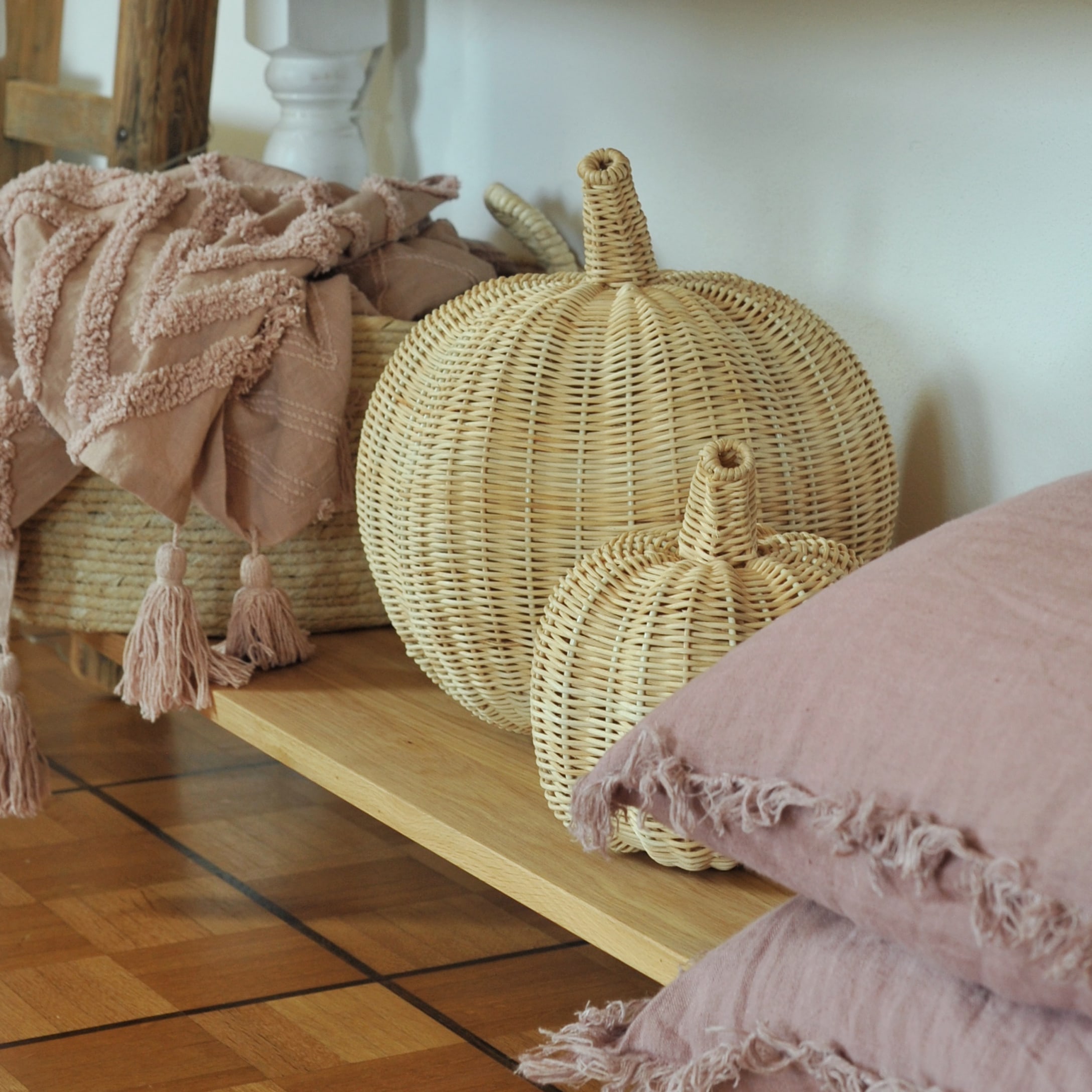 Decoratieve pompoenen van natuurlijk rattan op houten plank met roze kussens