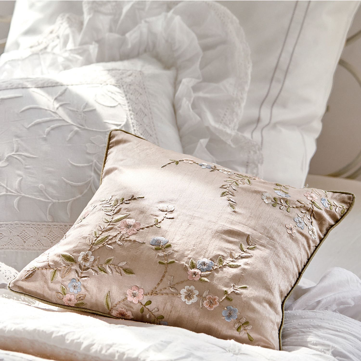Beige sierkussen met geborduurde bloemen op wit beddengoed, zachte stof