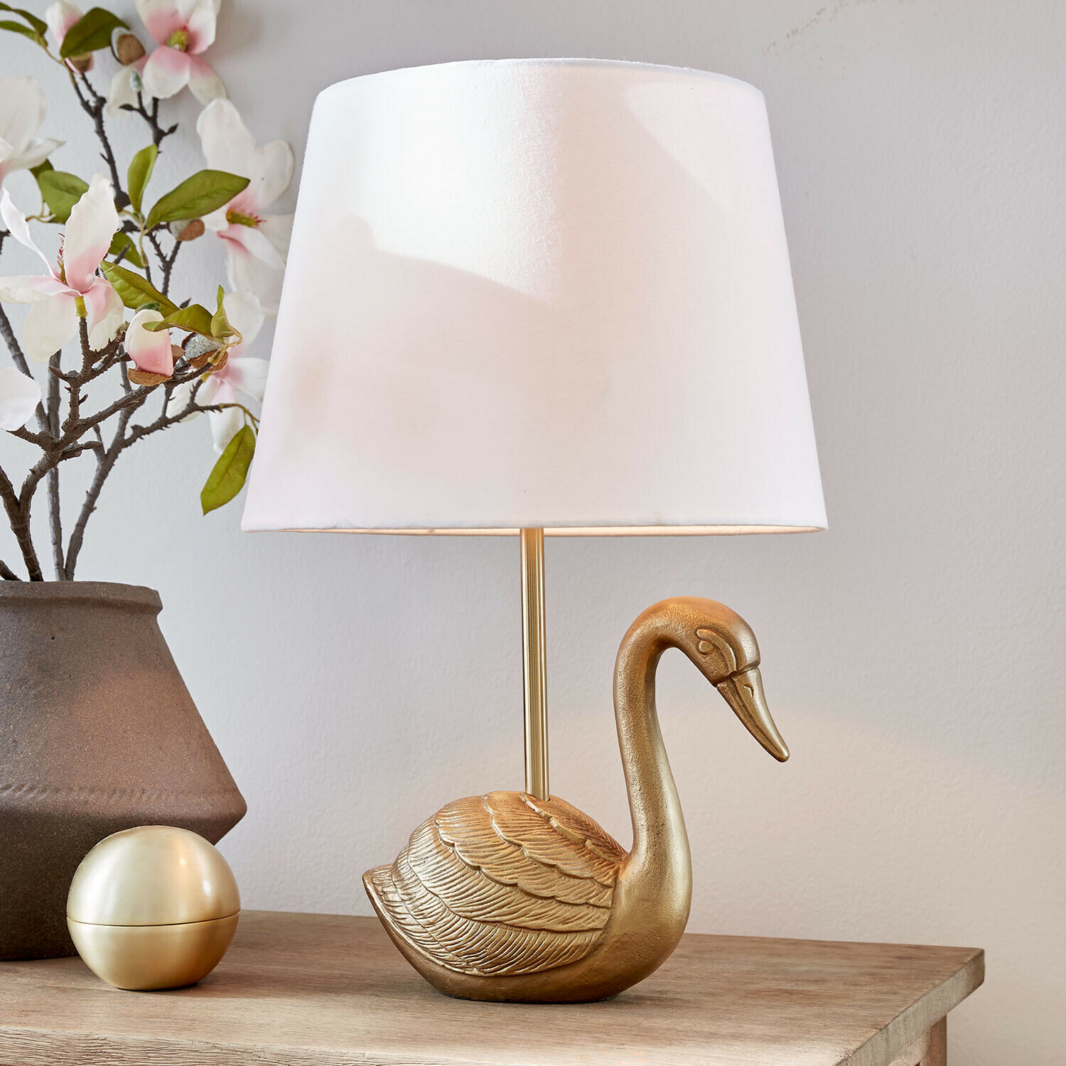 Gouden tafellamp in de vorm van een zwaan met witte kap op houten tafel met bloemendecoratie