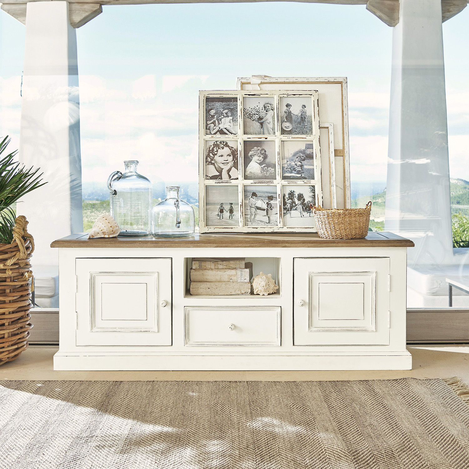Witte houten dressoir met lade en deuren, versierd met glazen flessen en vintage fotolijsten
