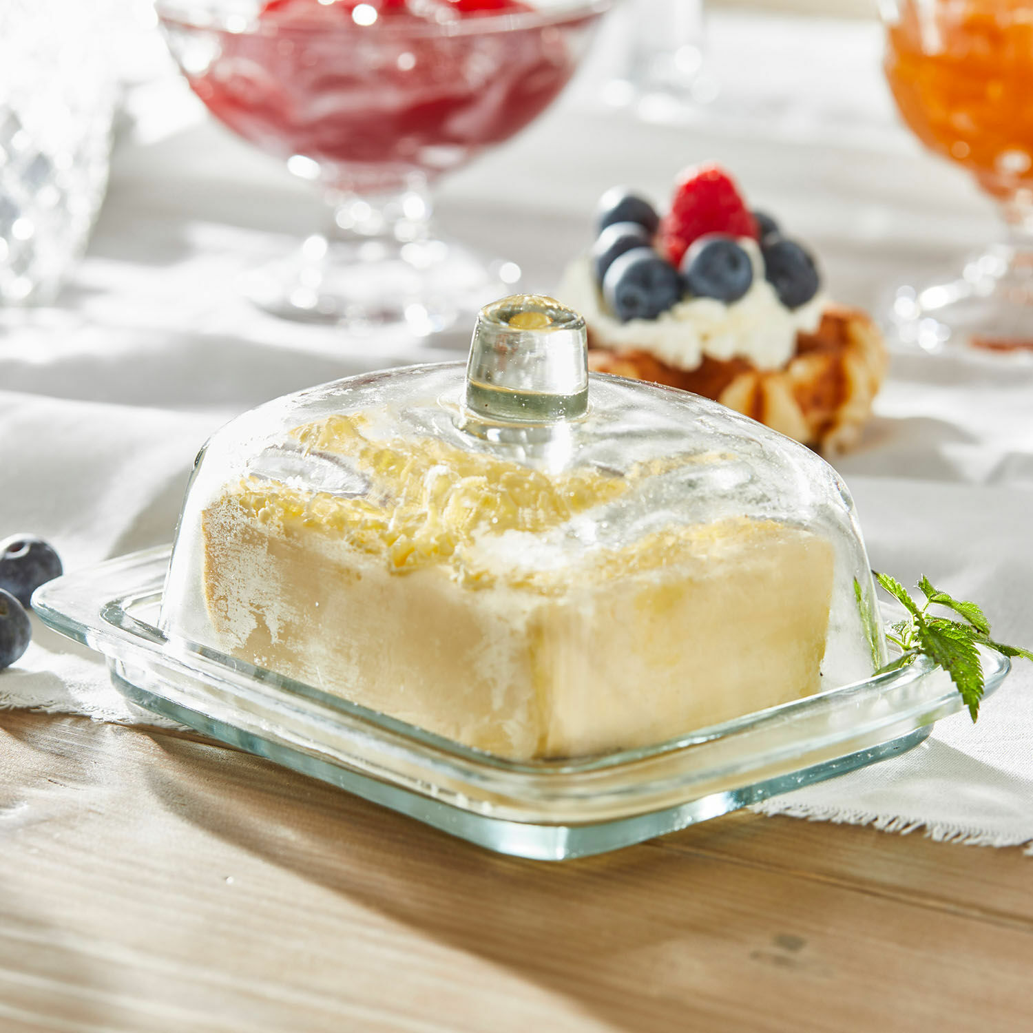 Glazen botervloot met doorzichtige deksel op houten tafel met boter erin