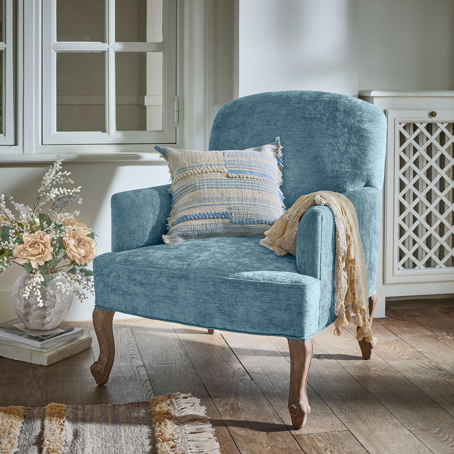 Blauwe gestoffeerde fauteuil met houten poten en decoratief kussen in een gezellige kamer