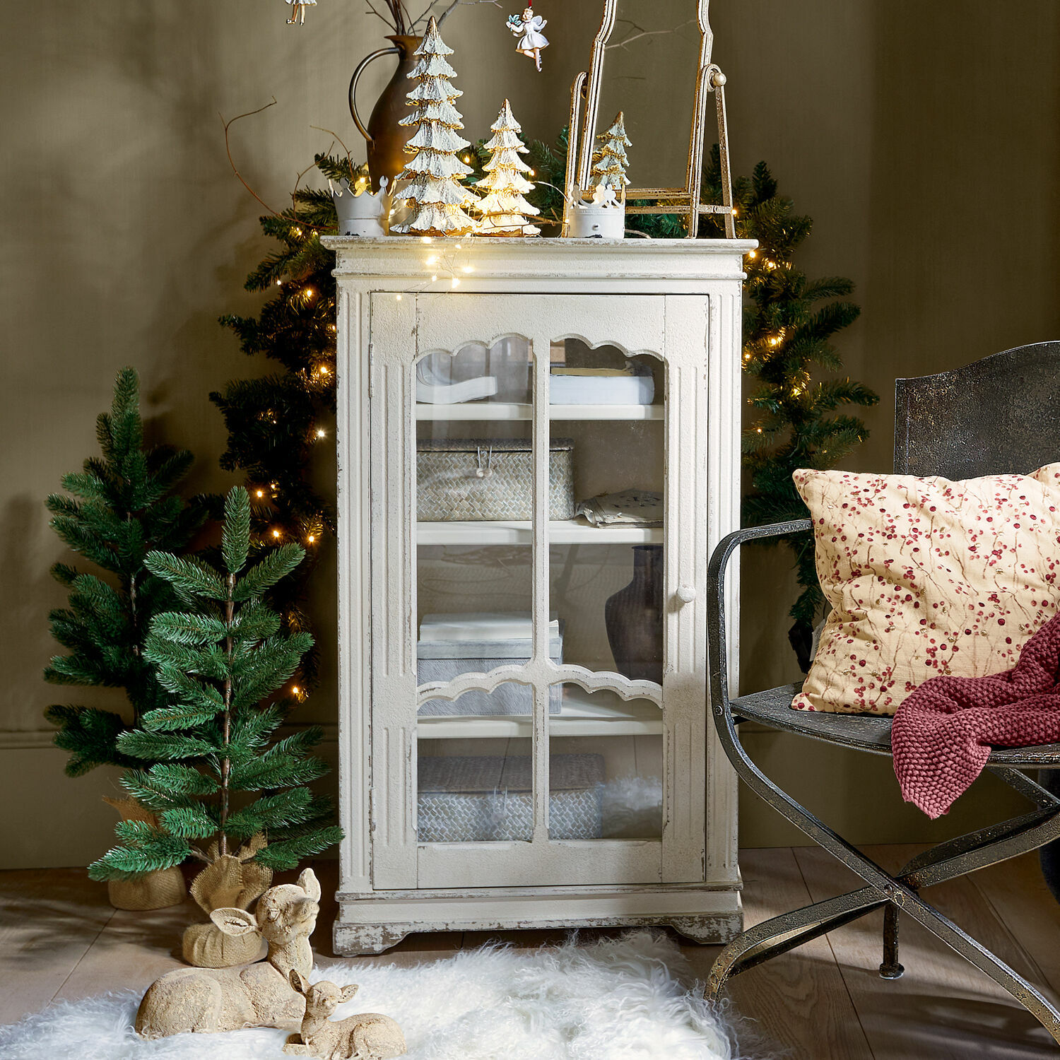 Witte houten vitrinekast in vintage stijl met glazen deur, kerstdecoraties en groene dennenbomen