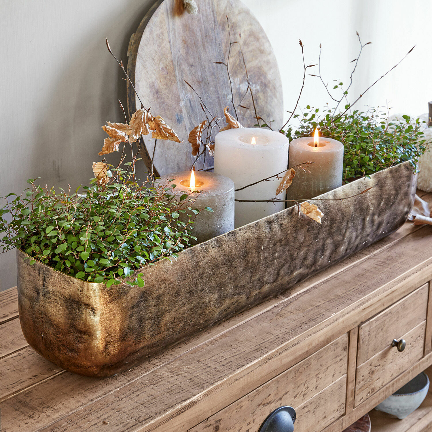 Decoratieve gouden metalen plantenbak met groene planten en drie kaarsen op houten tafel