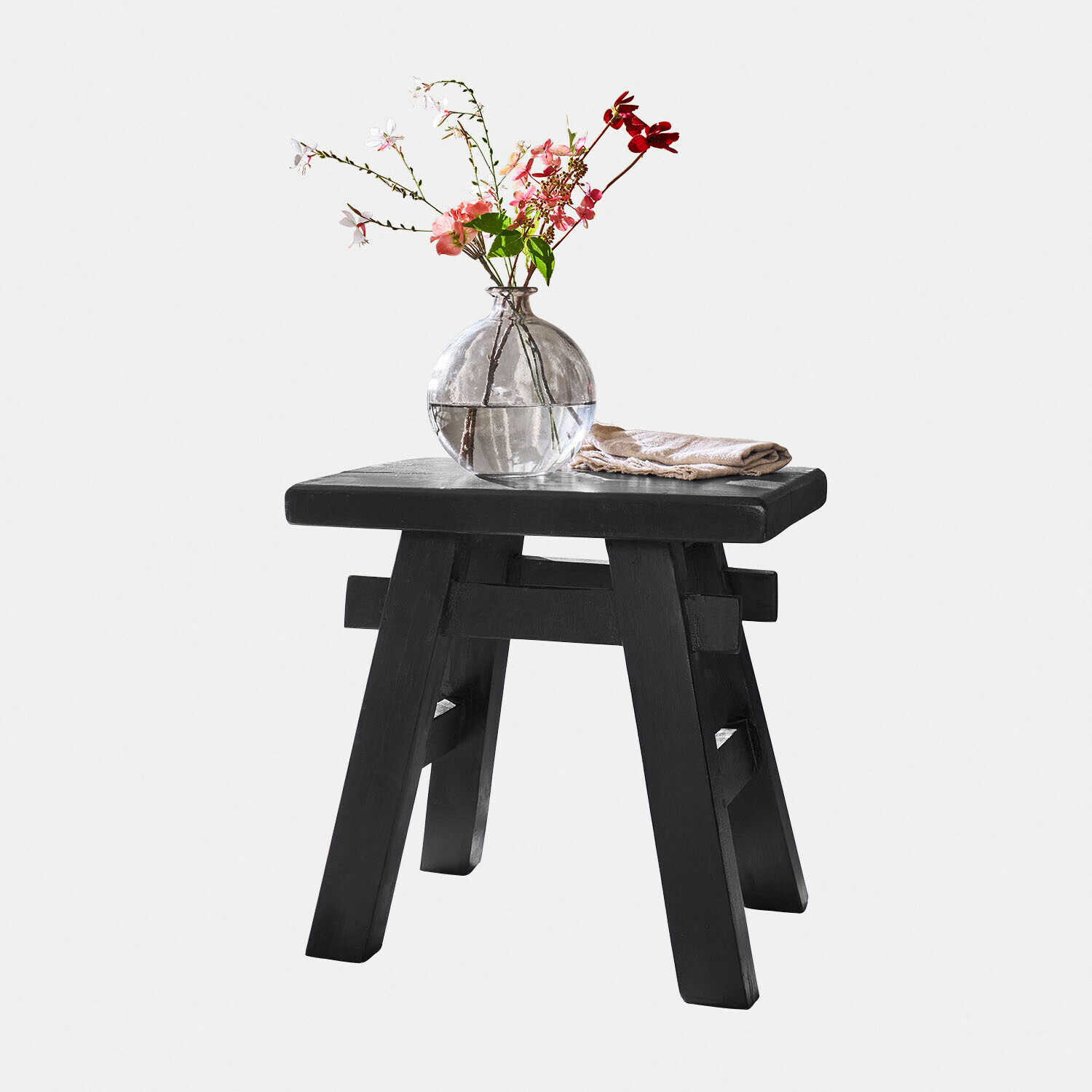 Zwarte houten kruk met ronde glazen vaas en bloemen, stijlvolle interieurdecoratie