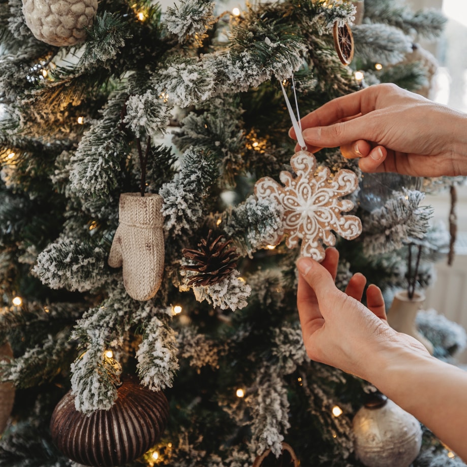 Handen hangen sneeuwvlokornament aan besneeuwde kerstboom met lichtjes en versieringen
