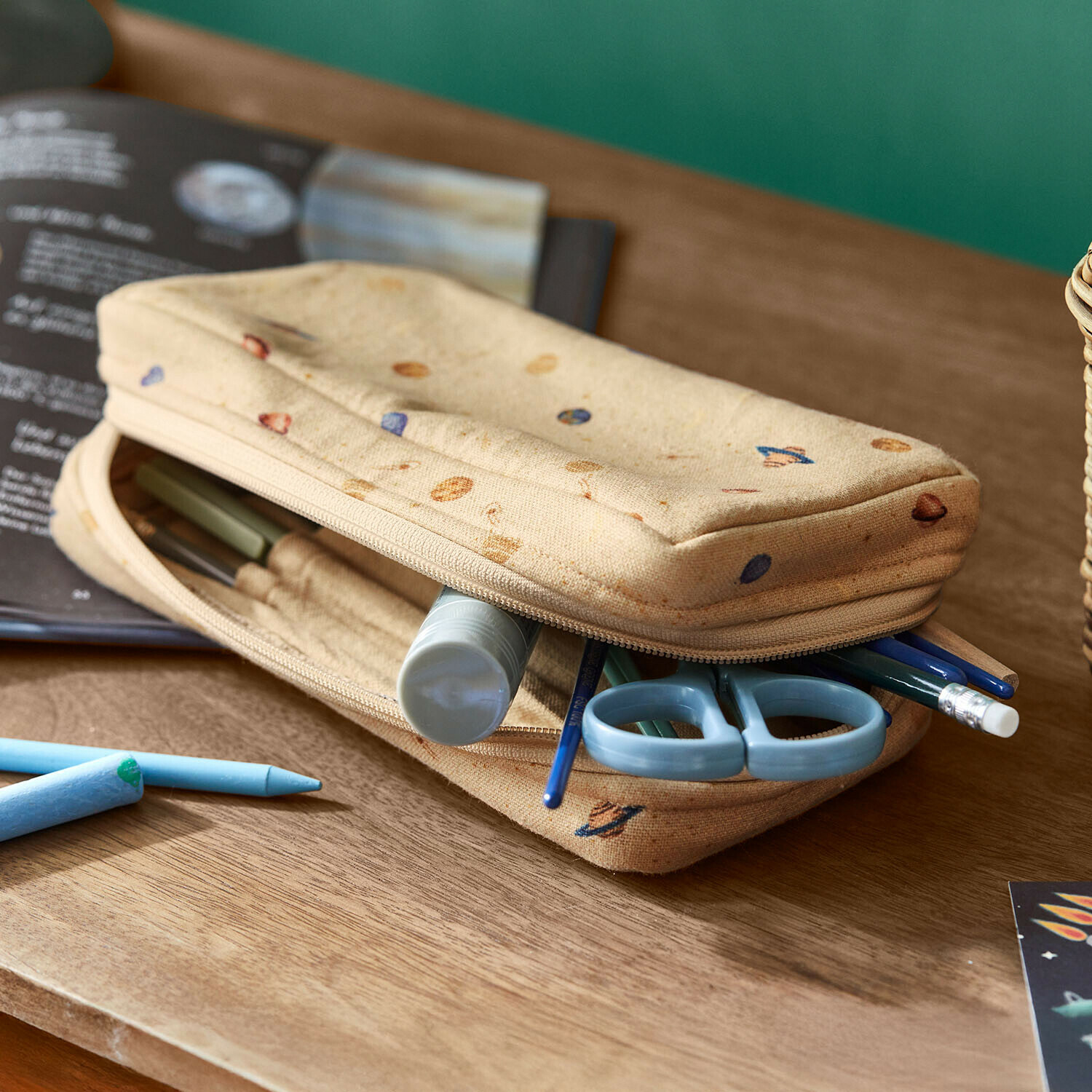 Beige stoffen etui met planetenmotief, blauwe schaar en schrijfwaren op houten bureau