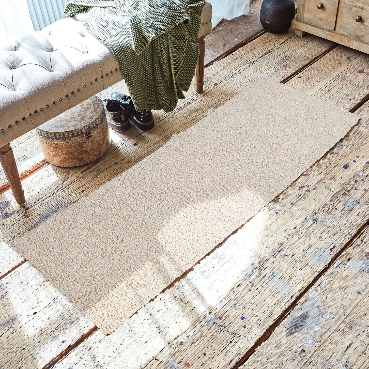 Loper Kaleema Beige vloerkleed van zacht materiaal op houten vloer in gezellige ruimte met bank en groene deken