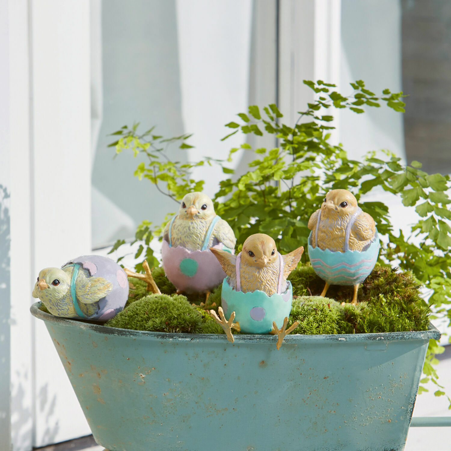 Decoratieve kuikenfiguren in pastelkleurige eierschalen op groen mos in een blauwe kruiwagen
