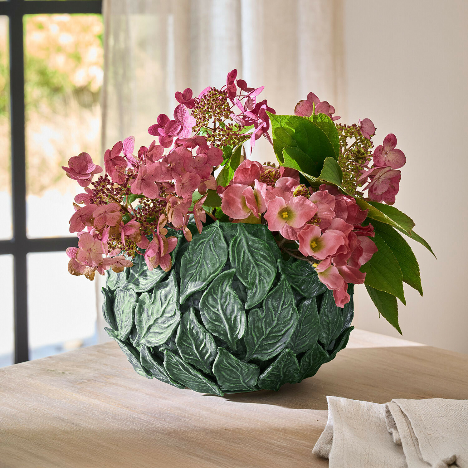 Groene decoratieve vaas met bladeren en roze bloemen op houten tafel in lichte kamer