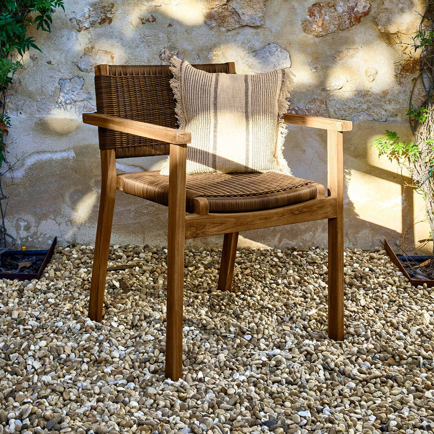 Tuinstoel van hout en riet in natuurlijke kleur met decoratief kussen op lichte kiezelgrond