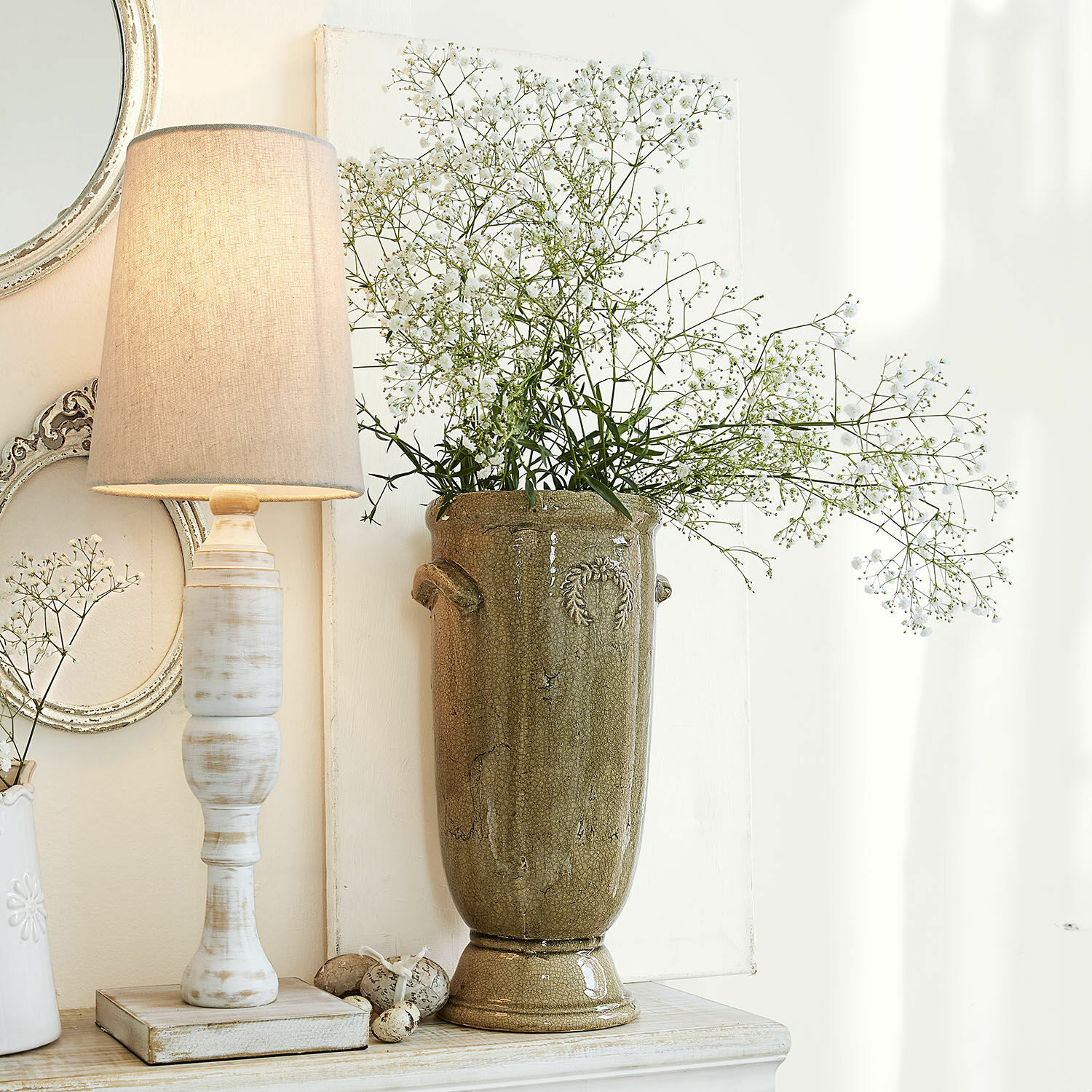 Hoge olijfgroene keramische vaas met fijne witte bloemen op lichte achtergrond