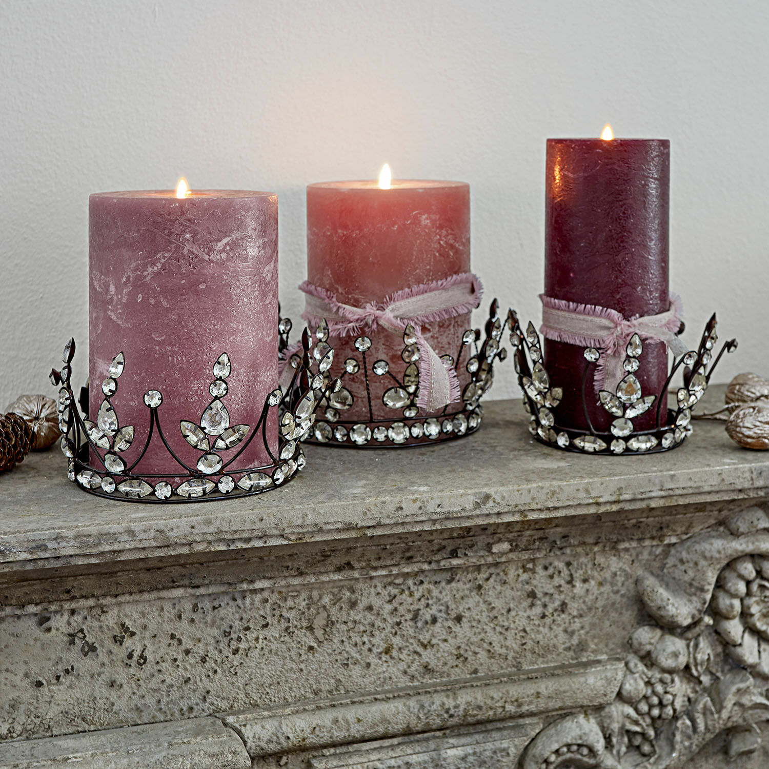 Drie roze decoratieve kaarsen met metalen houders versierd met kristallen op een stenen schoorsteenmantel