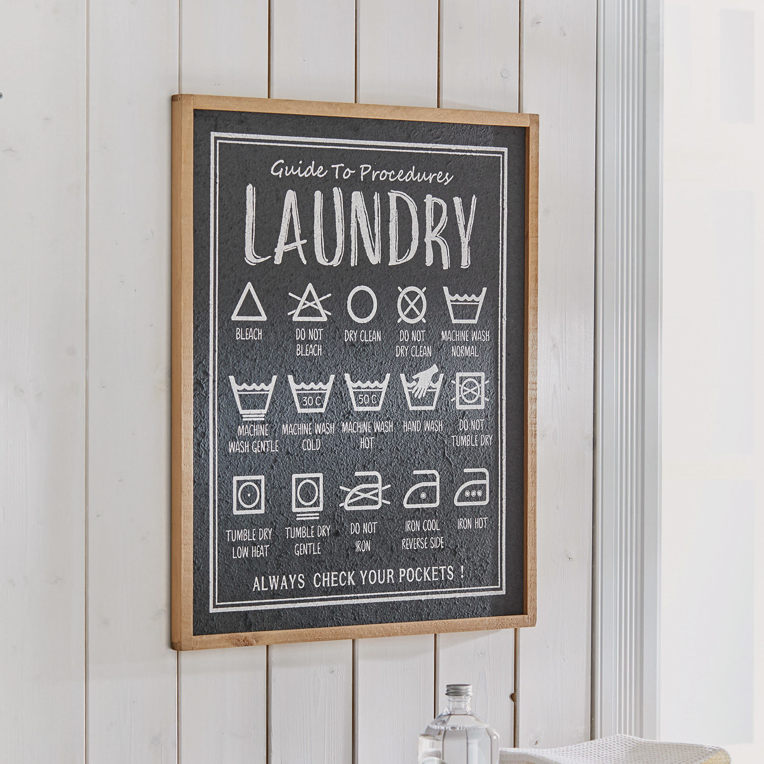 Decoratief bord met wasinstructies op zwarte achtergrond en houten lijst voor wasruimte