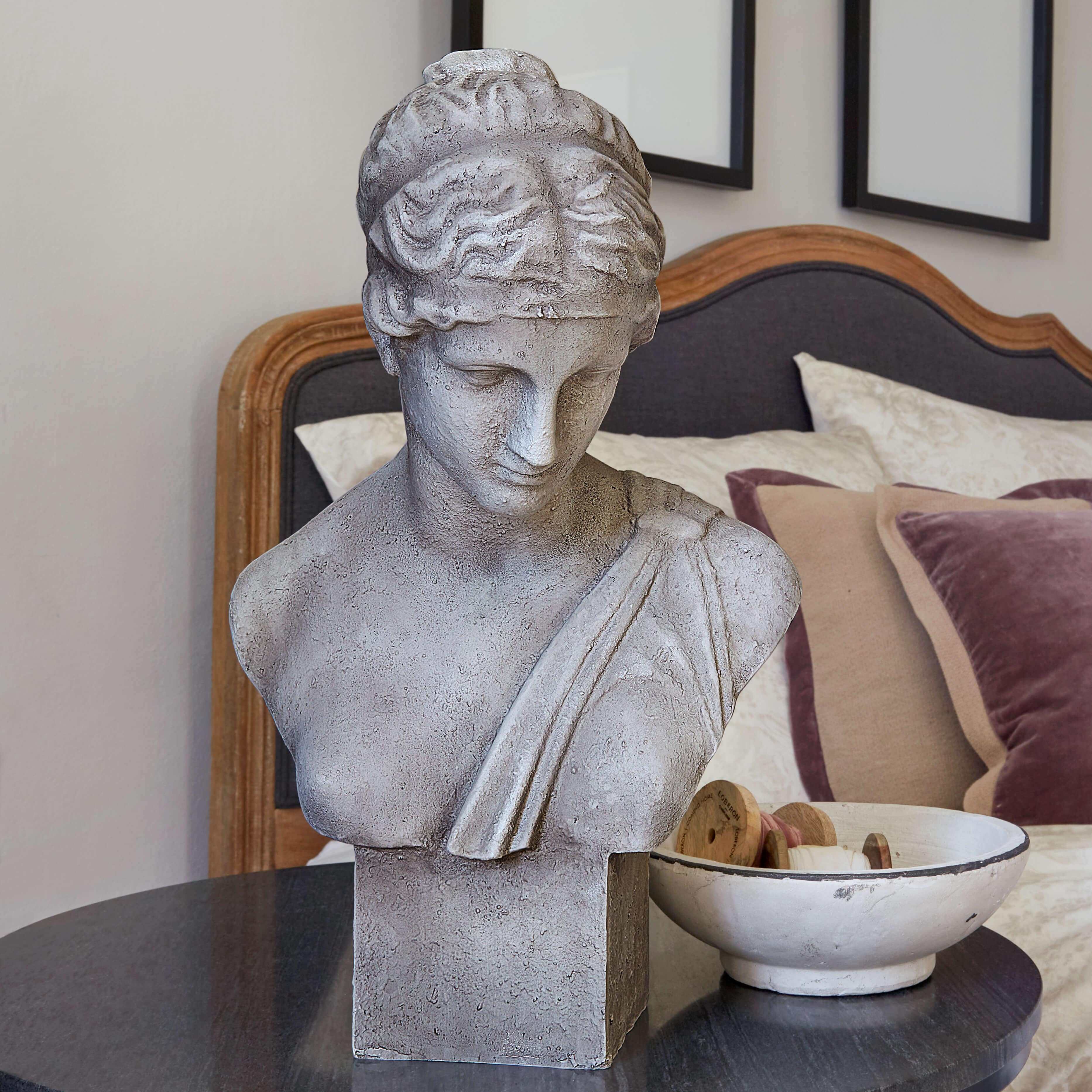 Grijs stenen buste op tafel naast witte kom met houten spoelen in slaapkamer