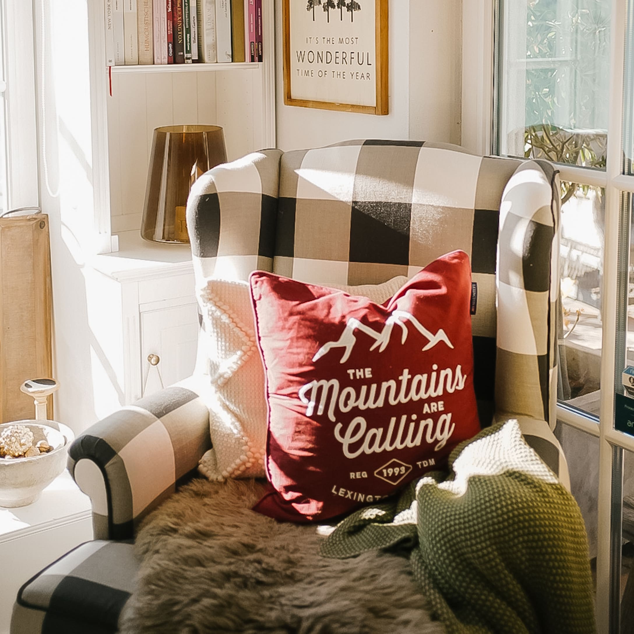 Geruite fauteuil met rode Mountains-kussen en zachte deken in lichte kamer