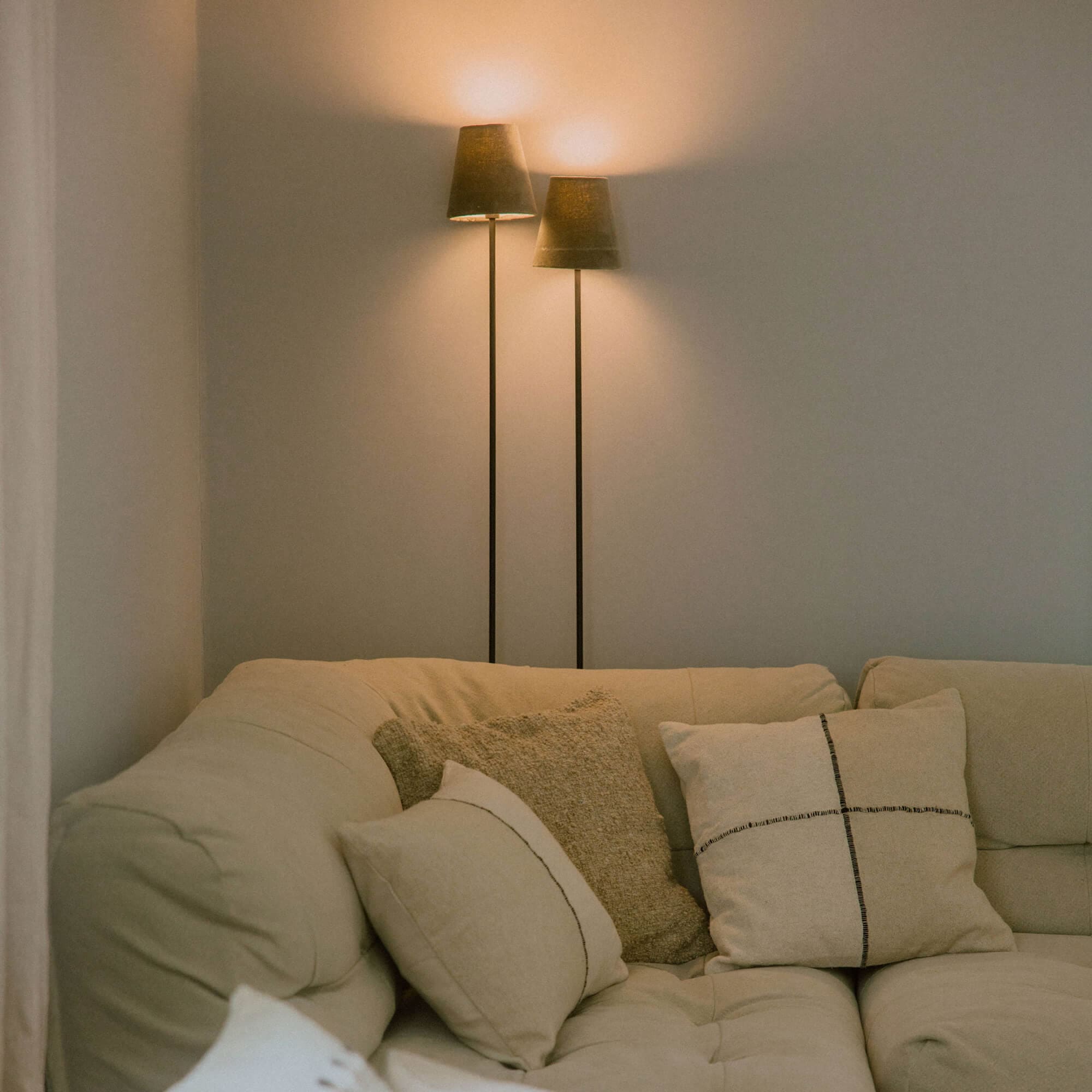 Beige bank met zachte kussens en twee staande lampen met donkere lampenkappen in de woonkamer