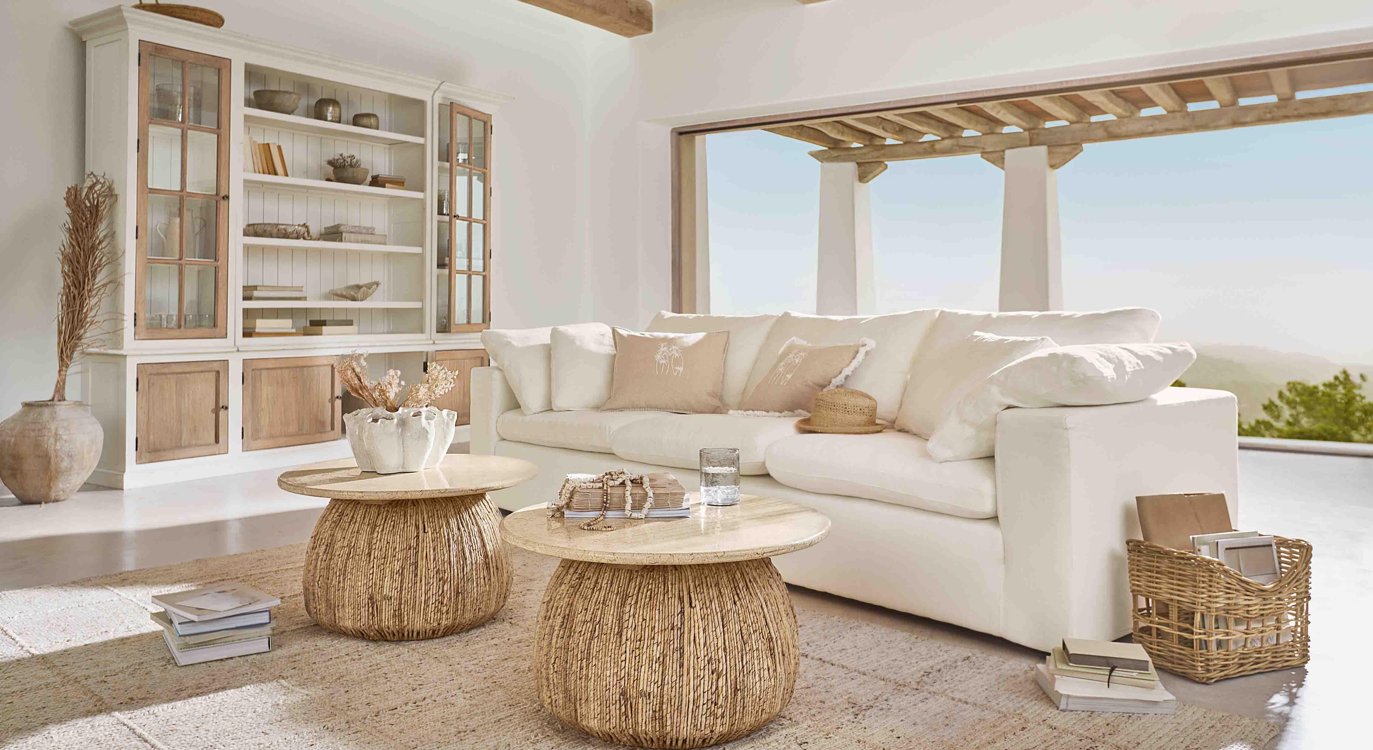 Gezellige woonkamer met witte bank en twee ronde salontafels van natuurlijk hout en riet