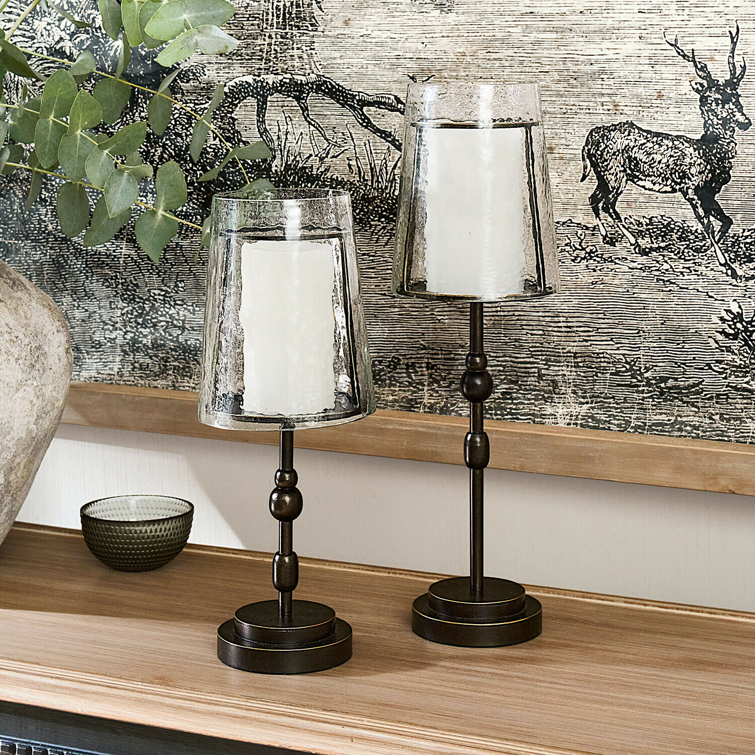 Kaarsenhouder set van 2 Hartcliff Twee metalen kandelaars met transparante glazen kappen en witte kaarsen op een houten blad