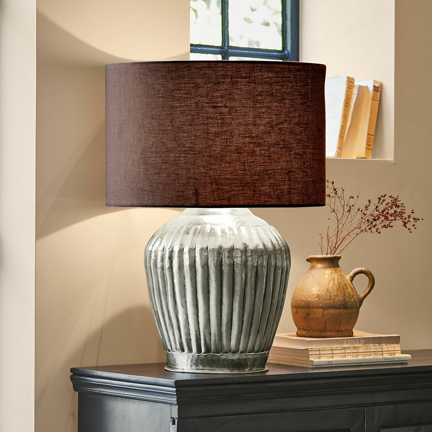 Tafellamp met zilverkleurige metalen voet en bruine kap op donkere kast