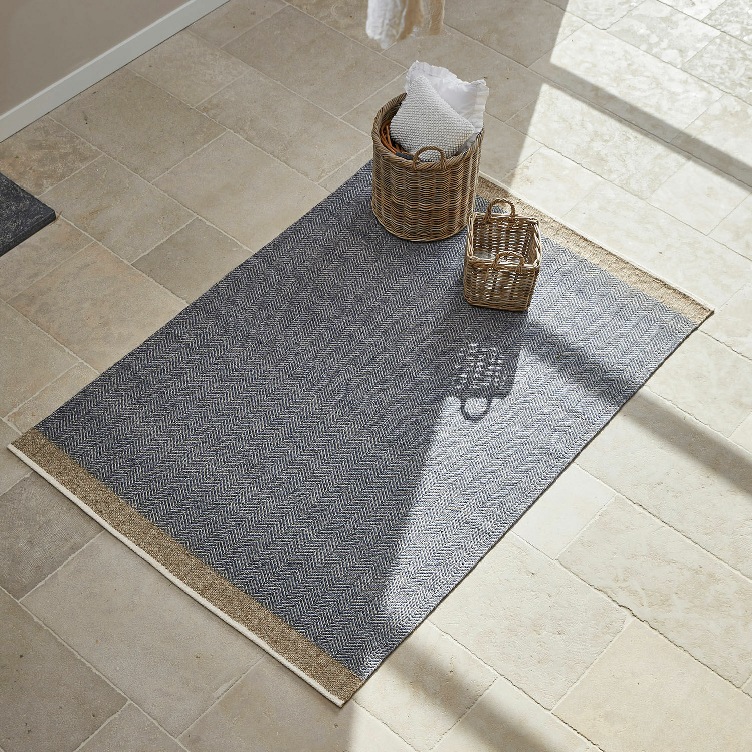 Grijs vloerkleed met visgraatpatroon en beige randen op lichte natuurstenen vloer