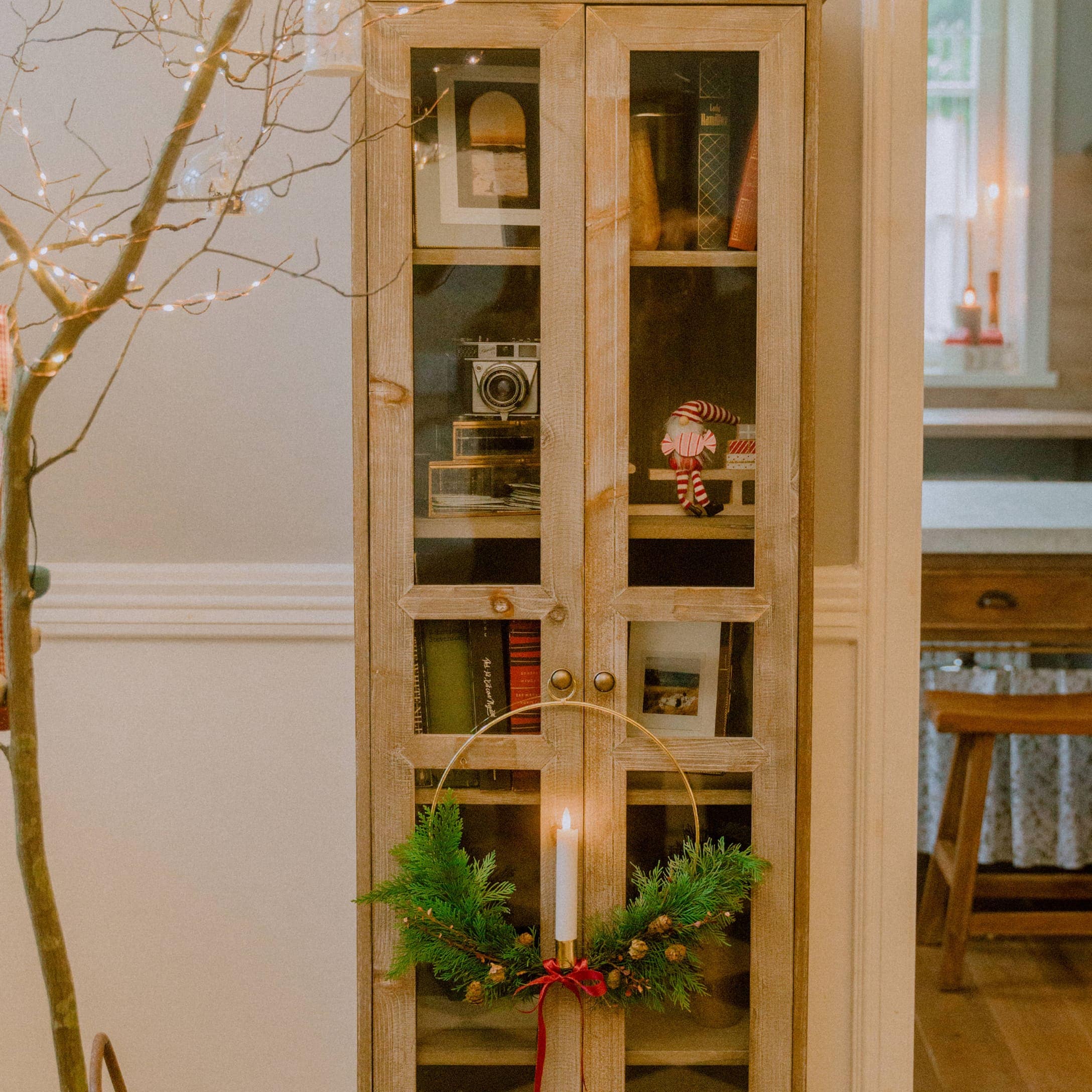 Houten vitrinekast met glazen deuren en kerstkandelaar met groene takken en rode strik