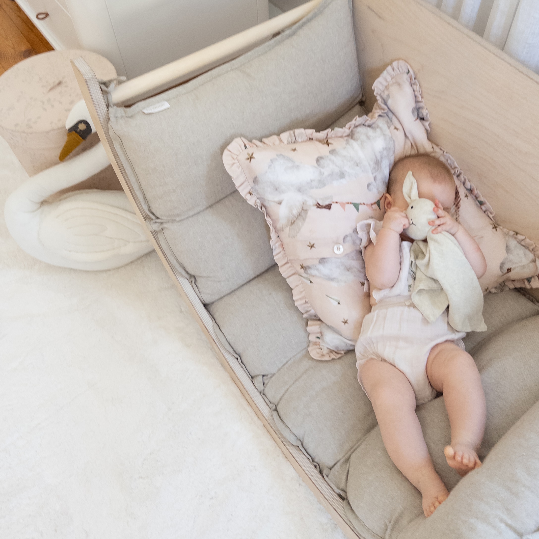 Baby liggend op zachte grijze matras met pastelgekleurde kussen en knuffelkonijn