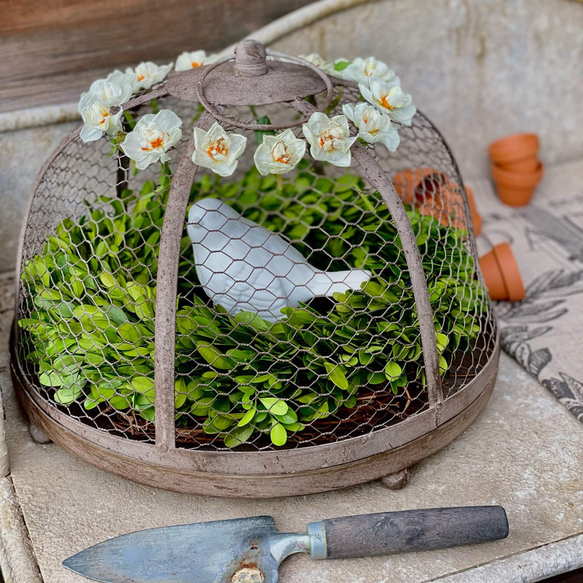 Metalen tuindecoratie met groen blad en witte keramische vogel onder bloemenkoepel