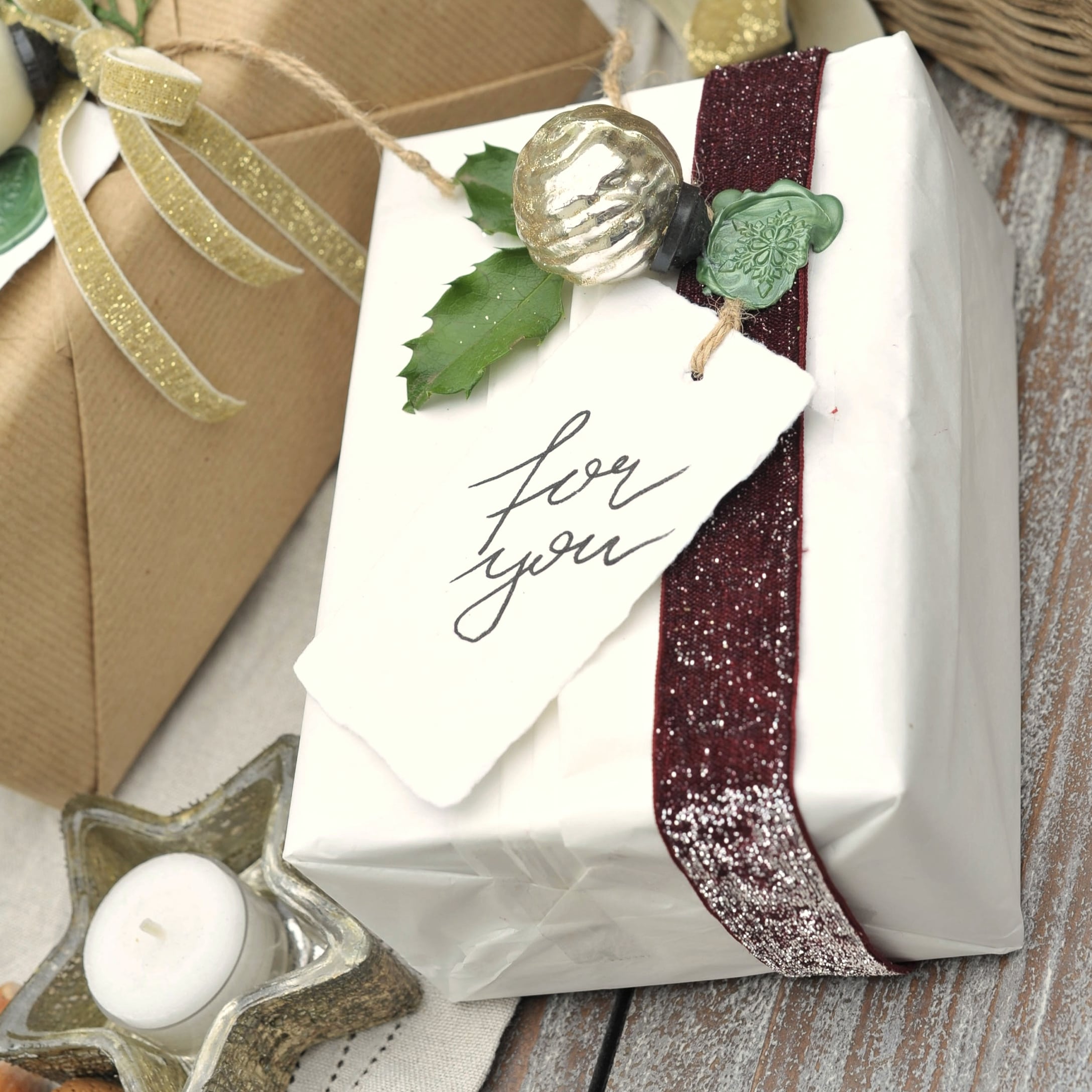 Cadeau verpakt in wit papier met bordeaux lint en groen blad, feestelijke kerstdecoratie