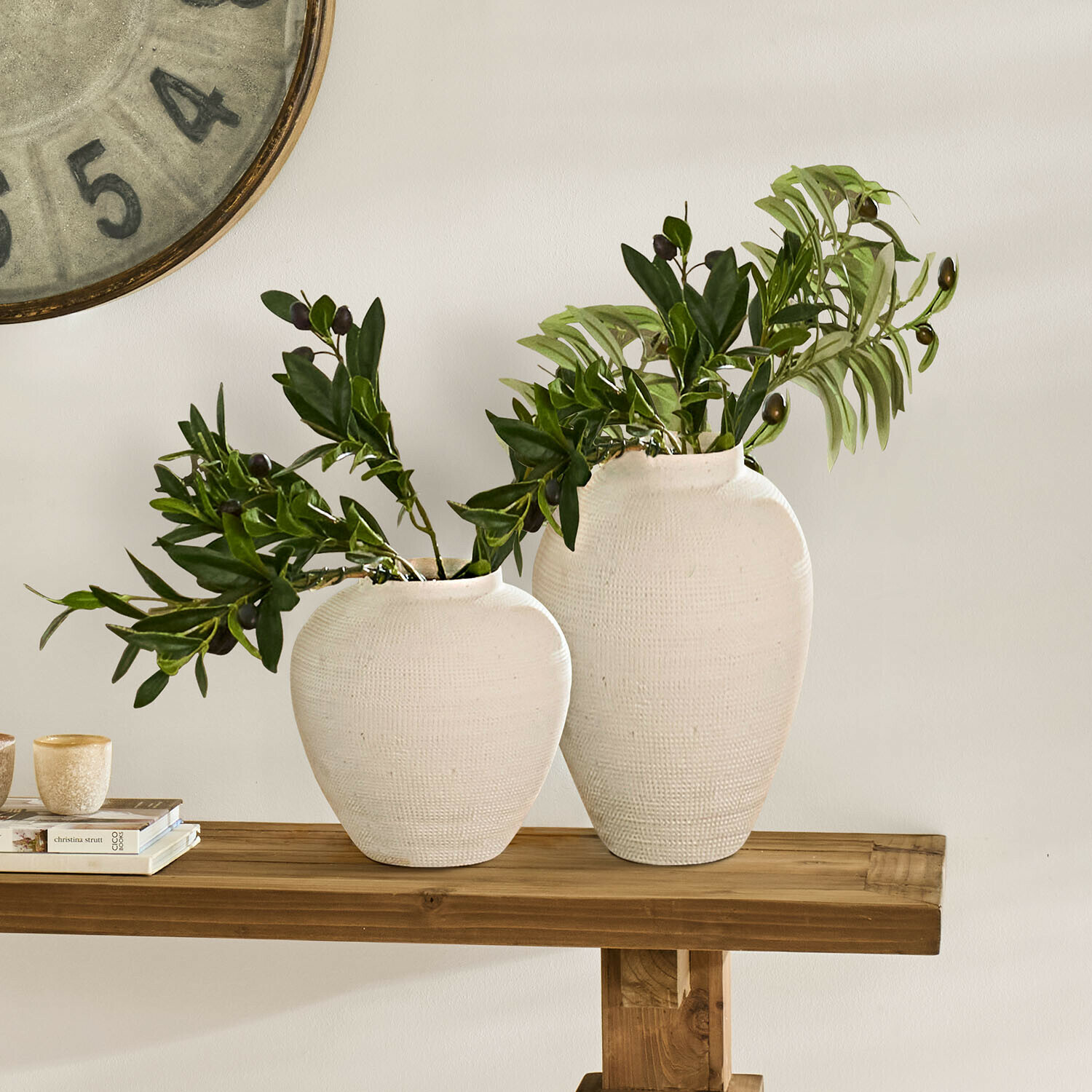 Twee witte keramische vazen met groene bladeren op een houten tafel, interieurdecoratie