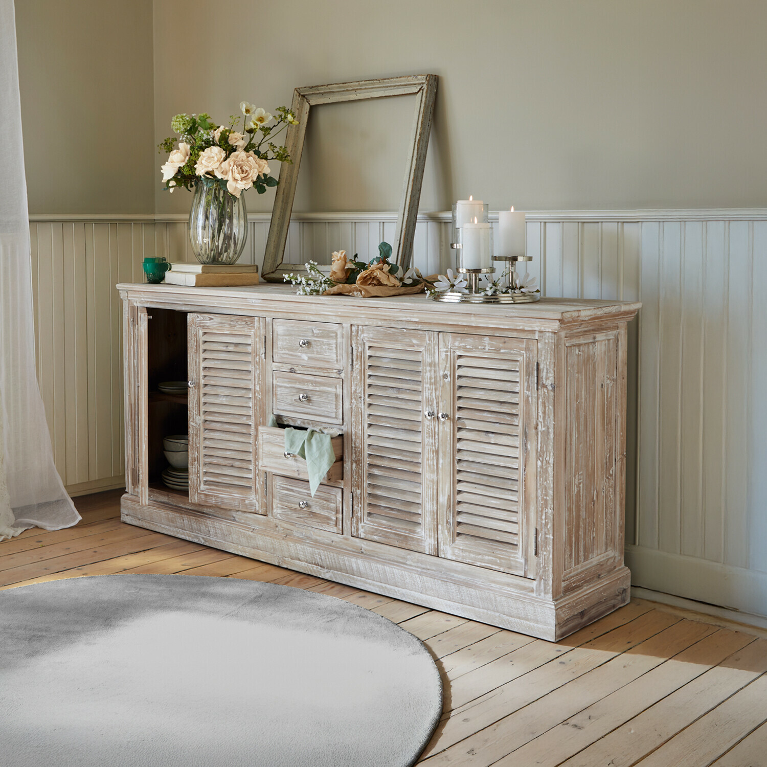 Buffetkast Houston Rustieke houten dressoir met witgewassen afwerking, bloemen en kaarsen in een woonkamer