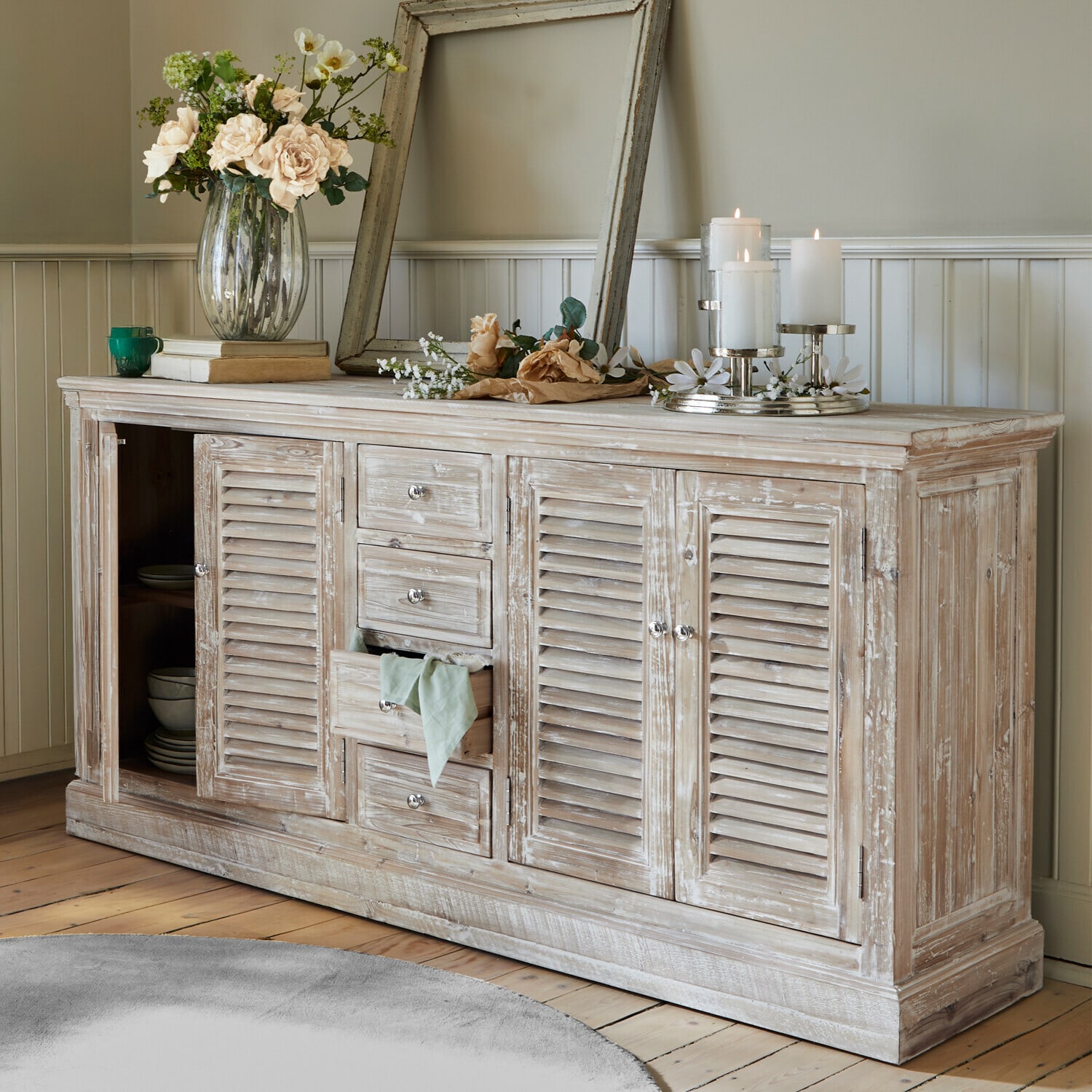 Buffetkast Houston Rustieke houten dressoir met witgewassen afwerking, bloemen en kaarsen in een woonkamer
