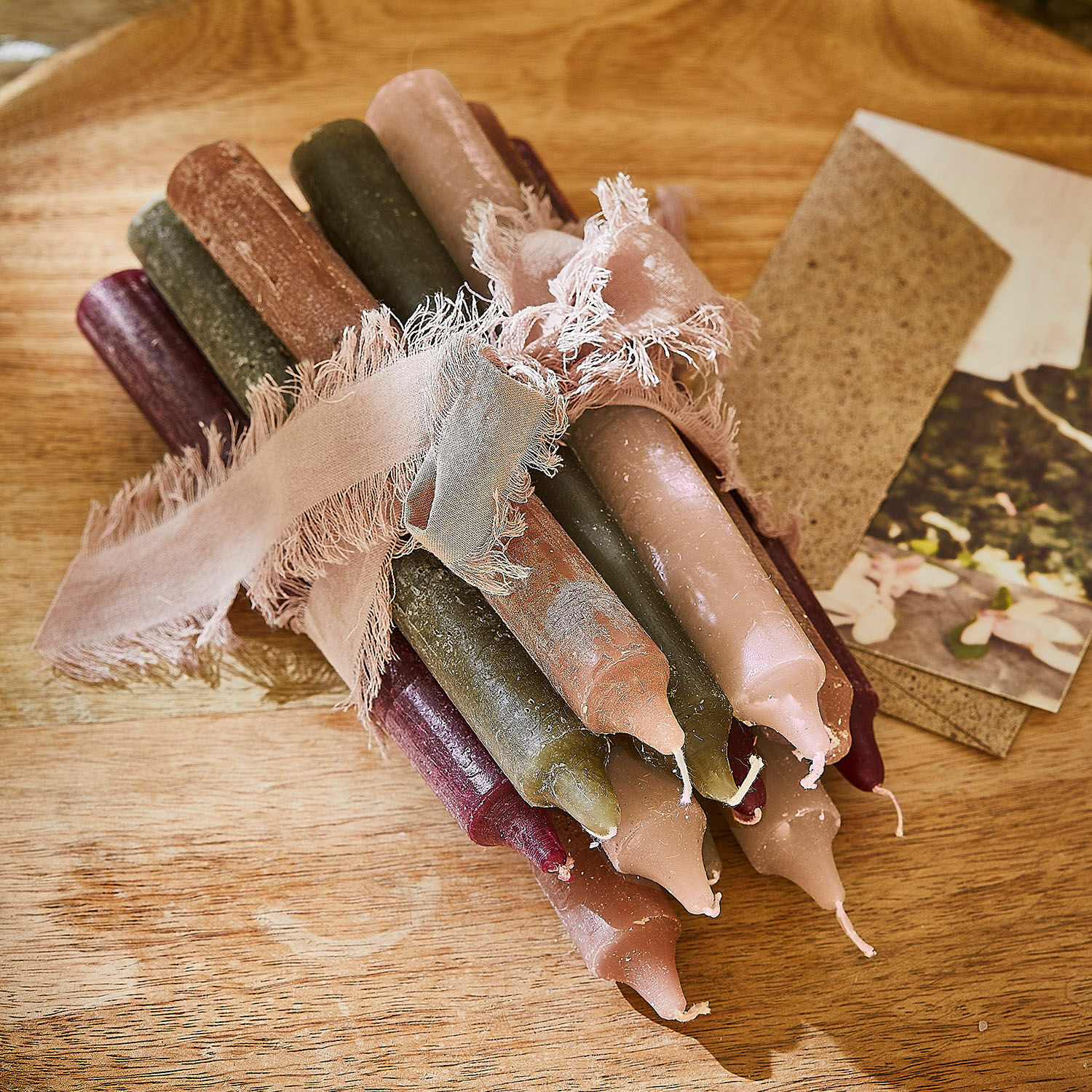 Set gekleurde tafelkaarsen van natuurlijke was gebonden met een roze lint op een houten tafel