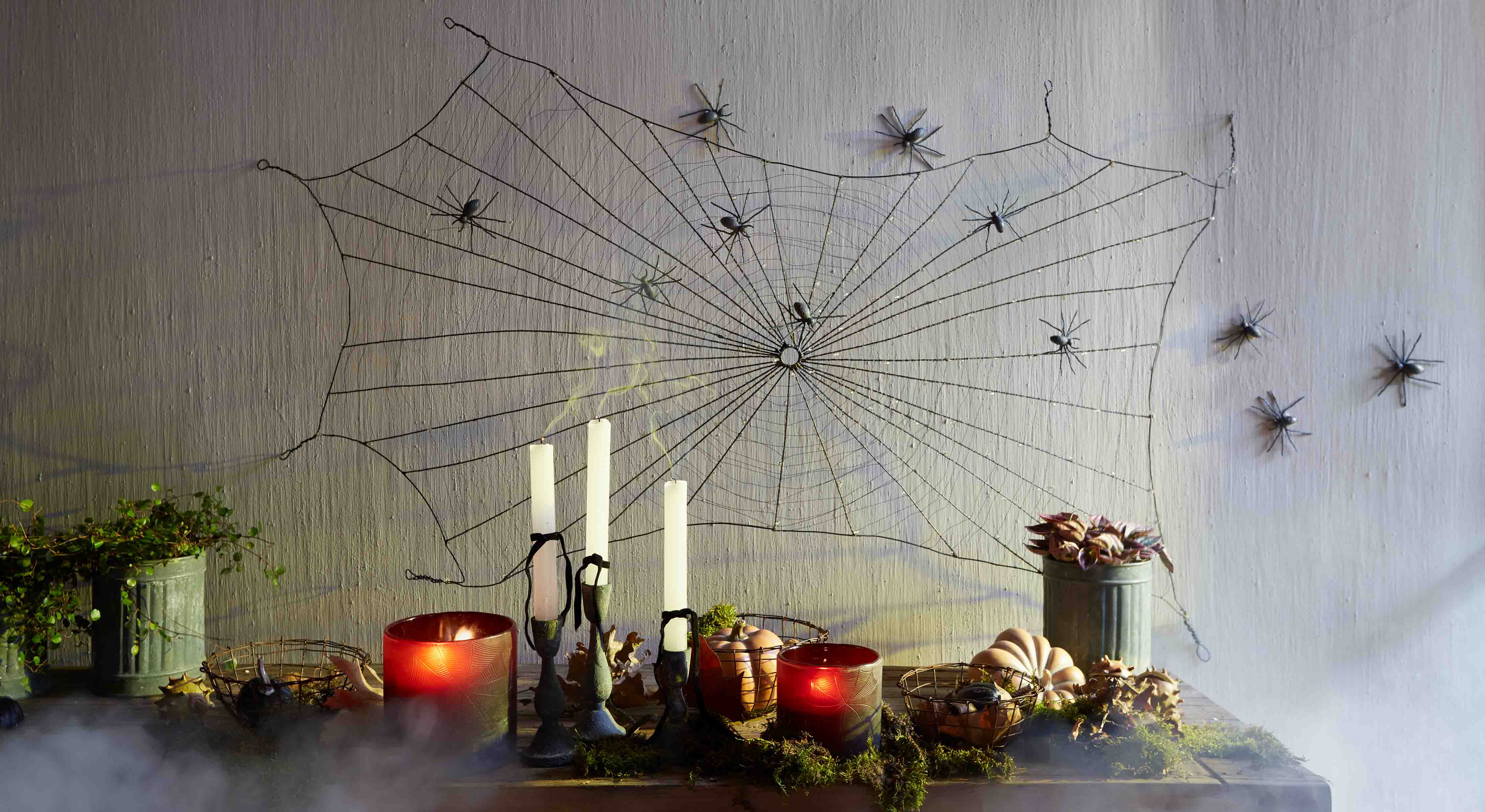 Halloweenversiering met zwart spinnenweb en plastic spinnen aan de muur, kaarsen en pompoenen op tafel