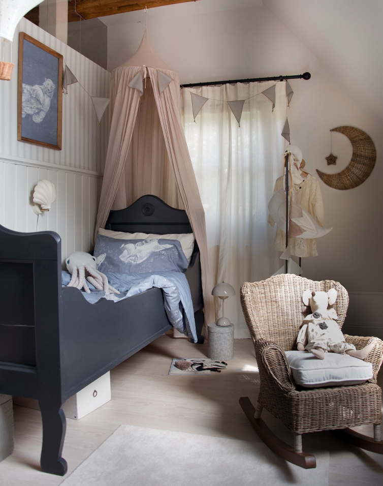 Gezellige kinderkamer met zwart bed, beige hemelbed en rotan schommelstoel