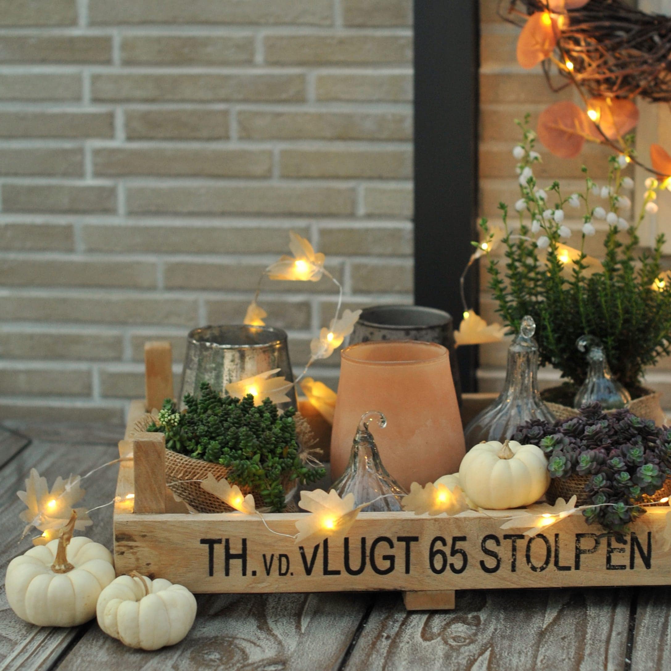 Houten dienblad met herfstdecoratie, witte pompoenen, planten en LED-lichtjes op tafel