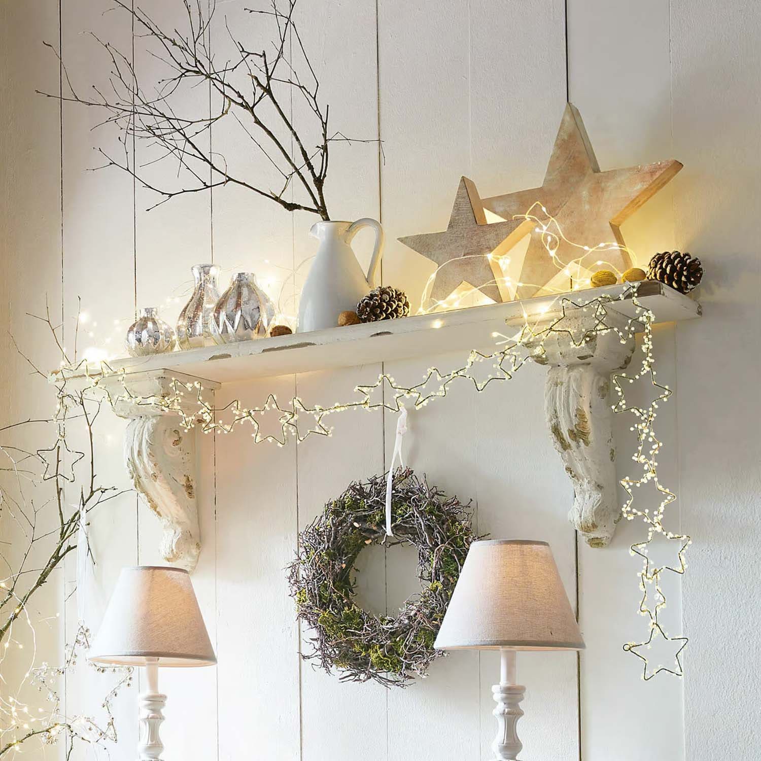 Witte houten decoratieve plank met stervormige lichtslinger, krans en tafellampen in landelijke stijl