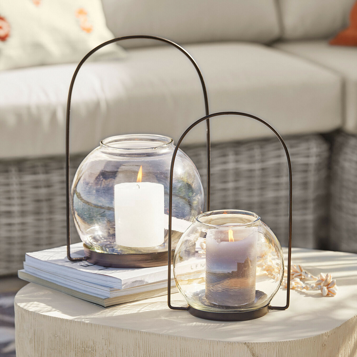 Windlicht set van 2 Serenaro Twee glazen lantaarns met metalen handvatten en brandende kaarsen op een lichte decoratieve tafel