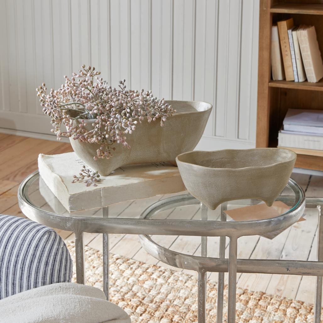 Twee beige keramische kommen op pootjes op een glazen tafel in een lichte, gezellige kamer